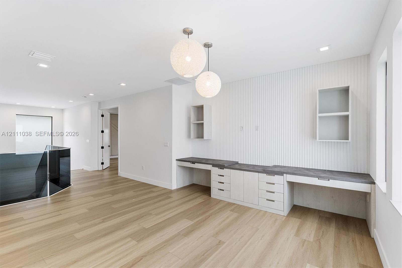 Built-in desk area with stone-finish countertops, vertical wall paneling, dual sphere pendant lighting, and wood-finish flooring