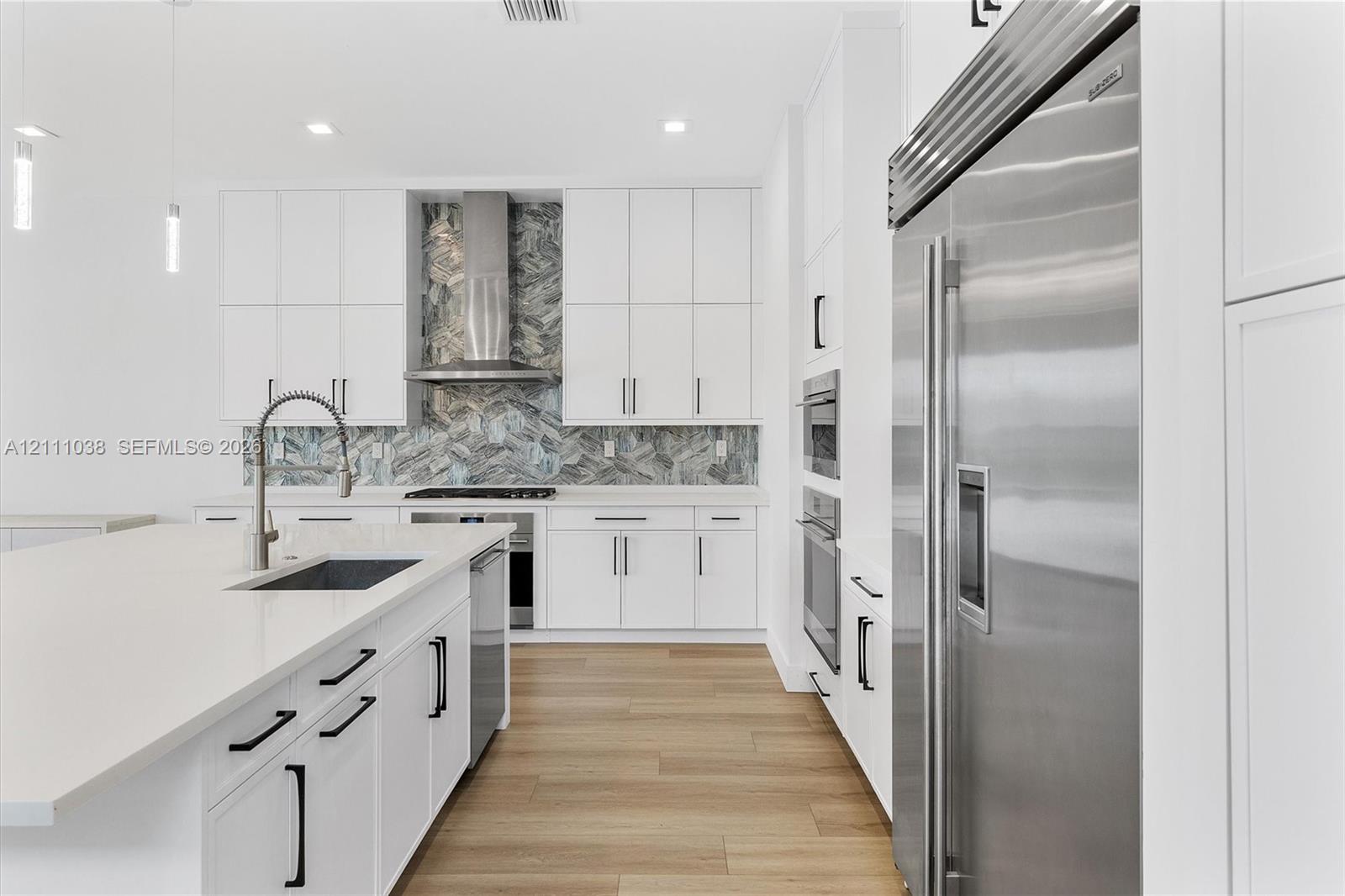 Kitchen featuring white cabinetry, wood-finish flooring, a herringbone-patterned stone backsplash, stainless steel appliances, and a quartz-topped center island