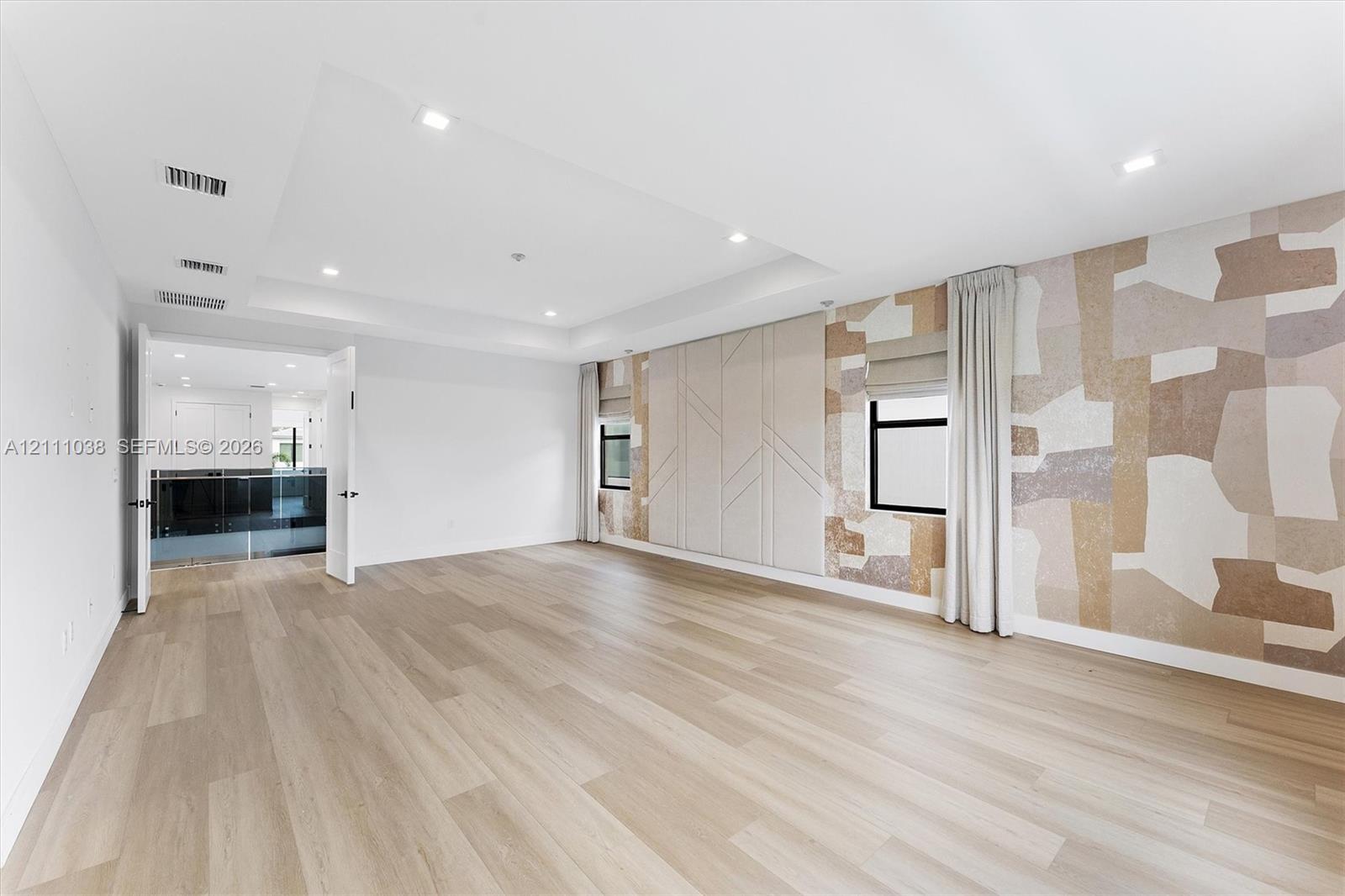 Tray ceiling with recessed lighting, wood-finish flooring, custom geometric wall paneling, and neutral-toned patterned wall covering