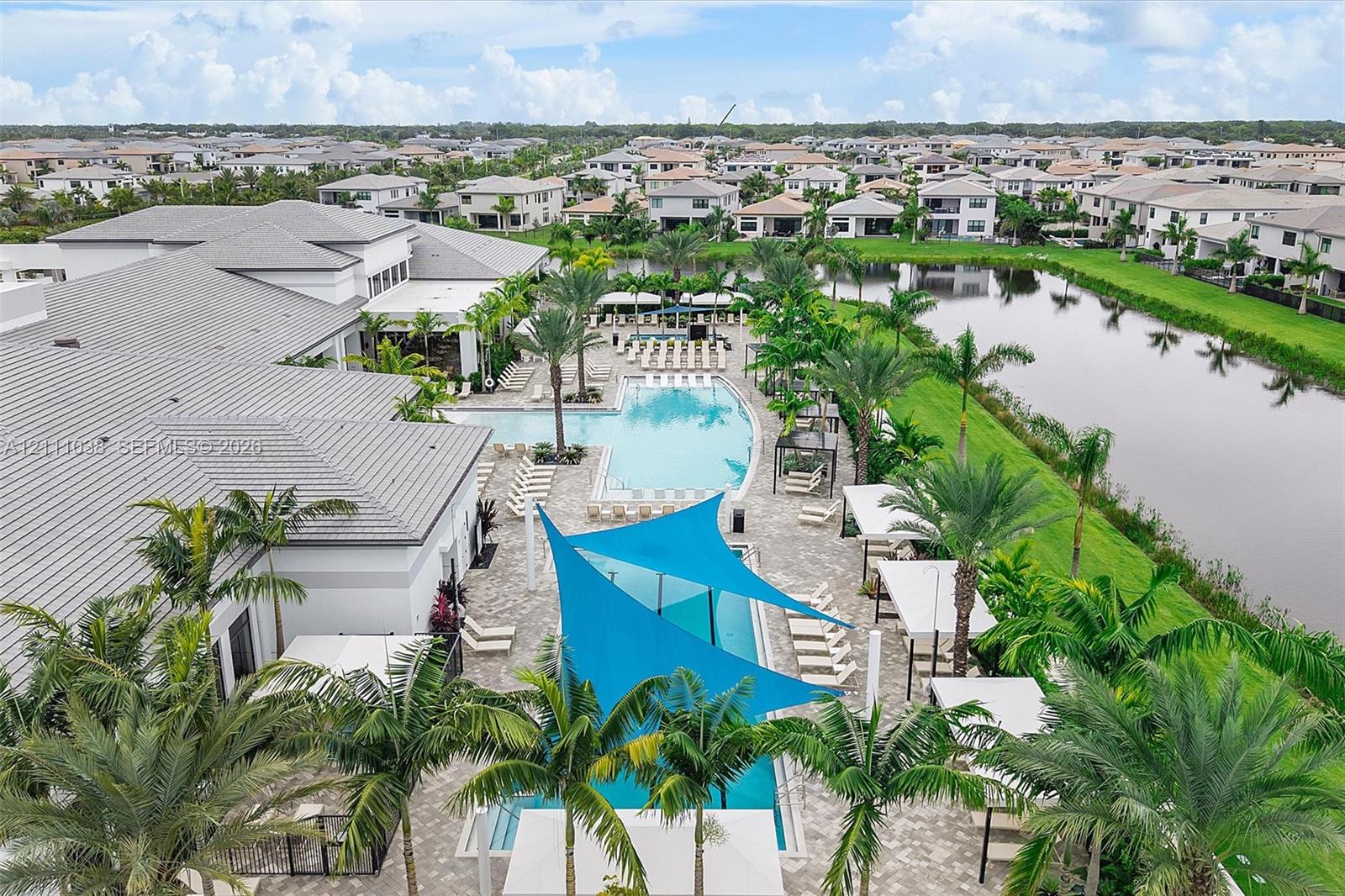 Resort-style swimming pool, expansive paver patio, integrated shade structures, tropical landscaping, and waterfront scenery