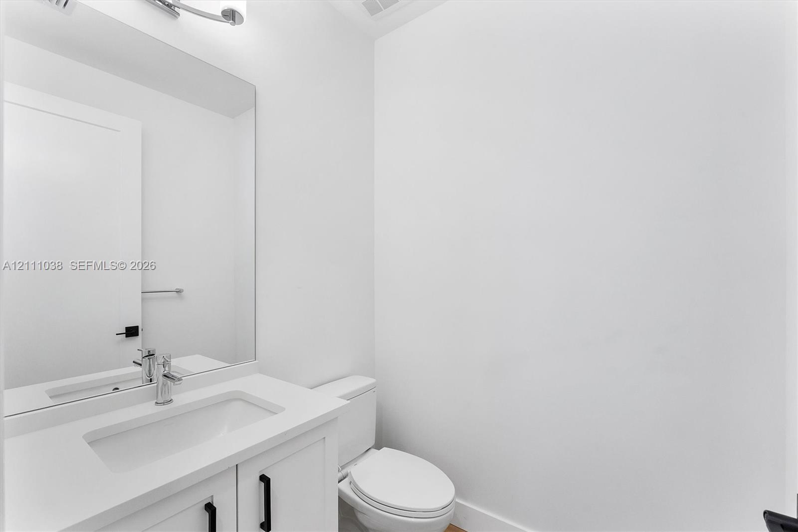 White vanity cabinet with a rectangular basin, quartz countertop, polished chrome faucet, large rectangular mirror, and matte black hardware