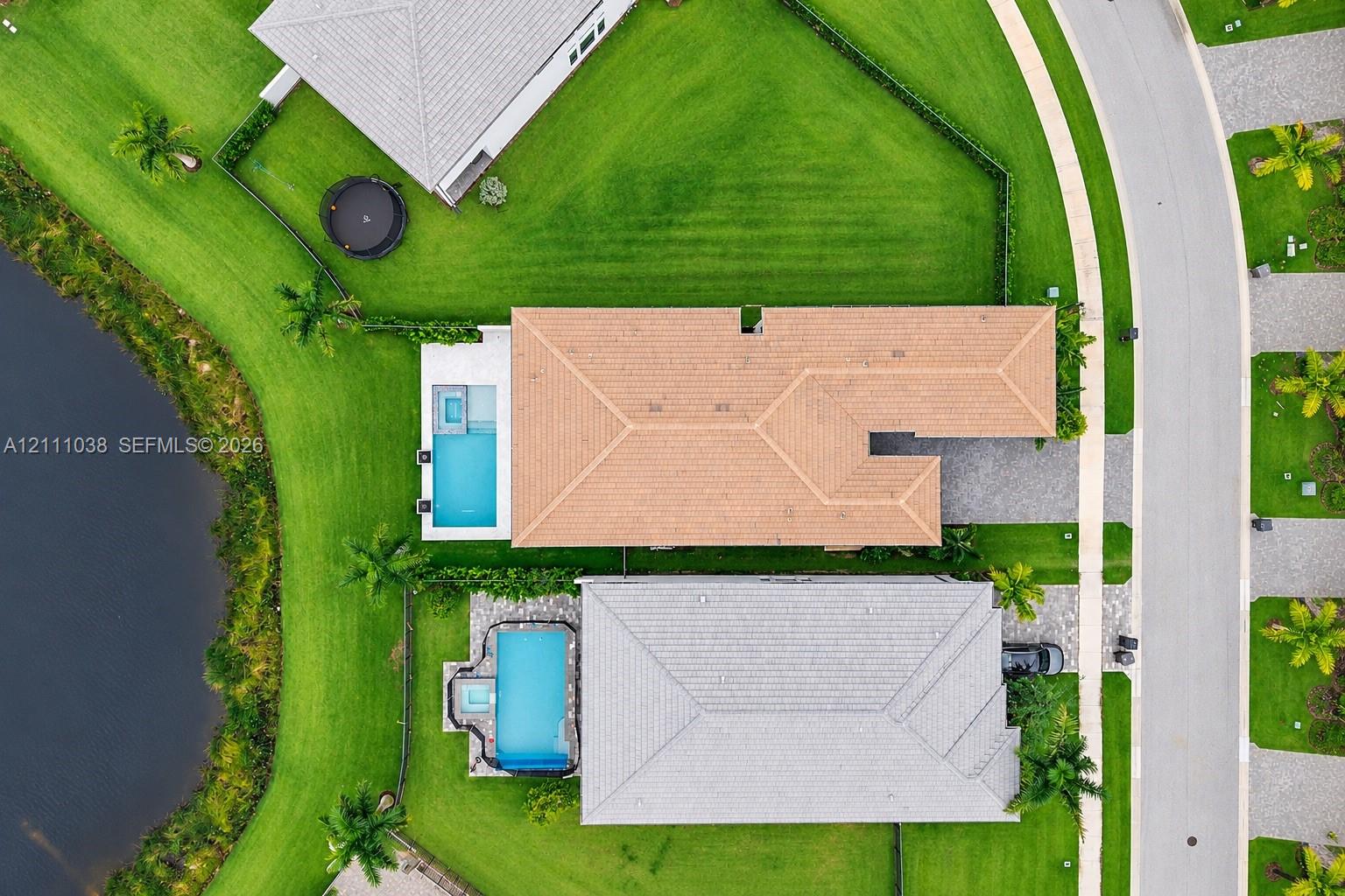 Aerial perspective featuring a tile-roofed residence, a rectangular swimming pool, an attached spa, paved driveway, and water frontage