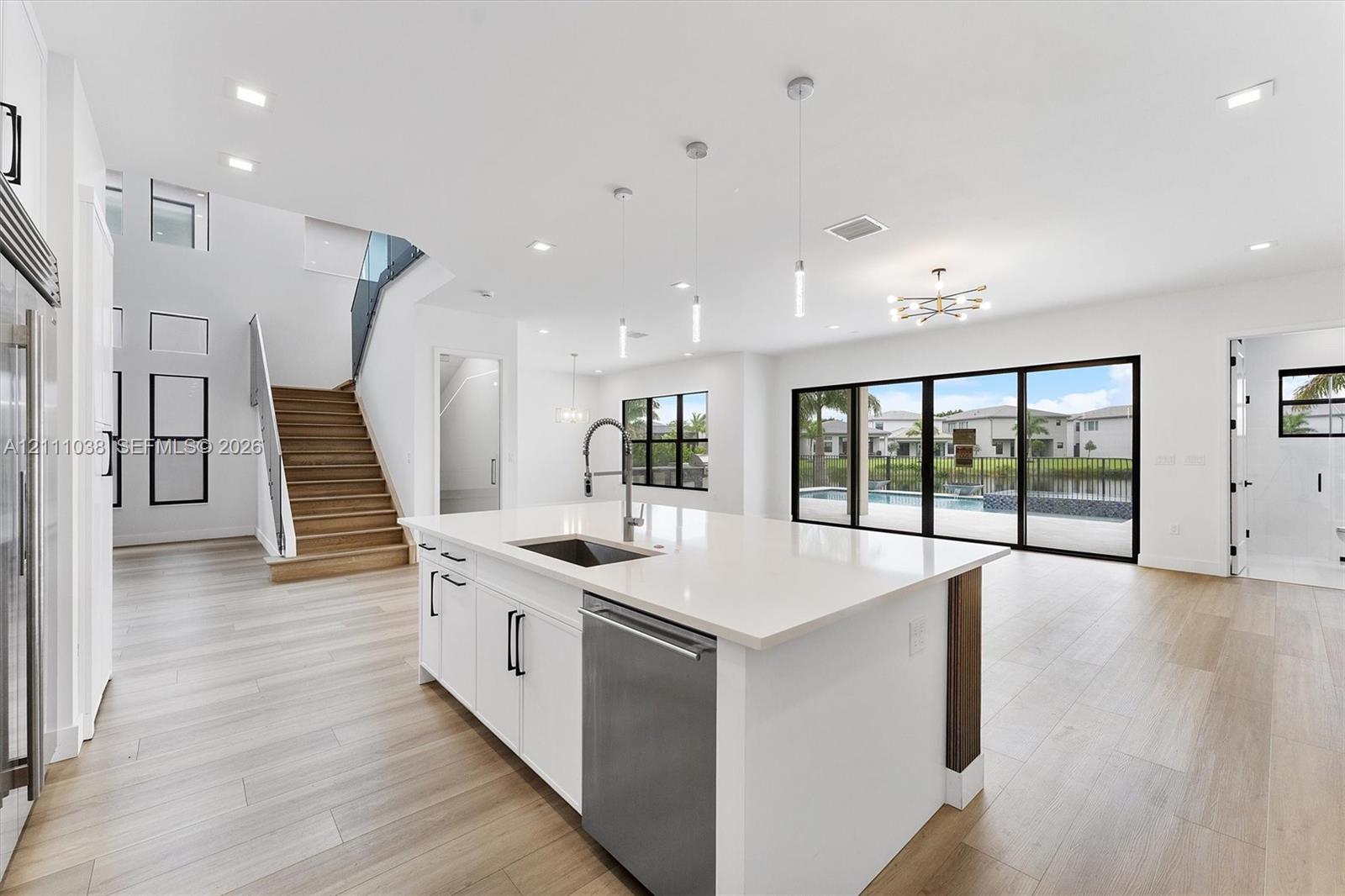 Open-concept kitchen featuring a center island with a quartz countertop, stainless steel dishwasher, and under-mount sink, complemented by wood-finish flooring, recessed lighting, and multi-panel sliding glass doors