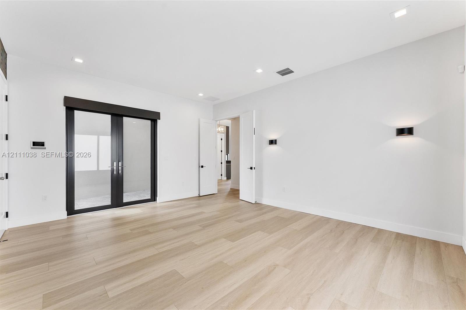 Room featuring light wood-finish flooring, recessed lighting, matte black wall-mounted fixtures, and glass-paned double doors with a dark frame