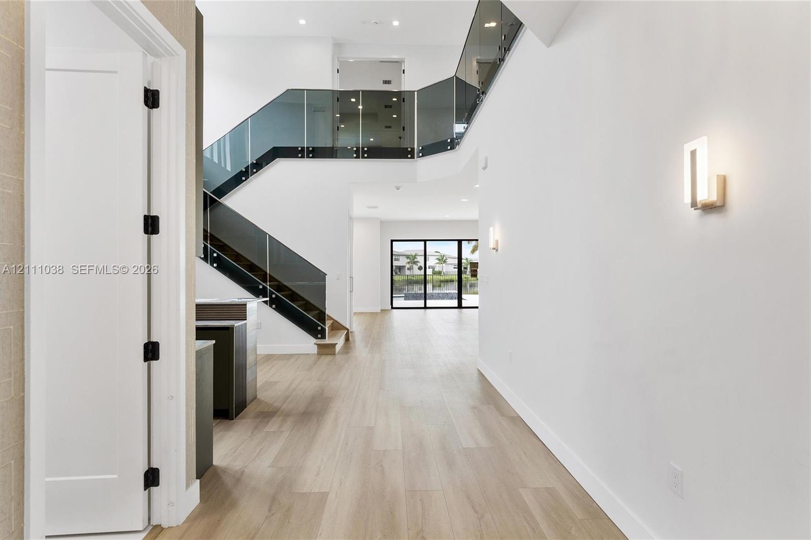 Two-story foyer featuring wood-finish flooring, a glass-paneled staircase with metal hardware, recessed lighting, and modern wall-mounted light fixtures