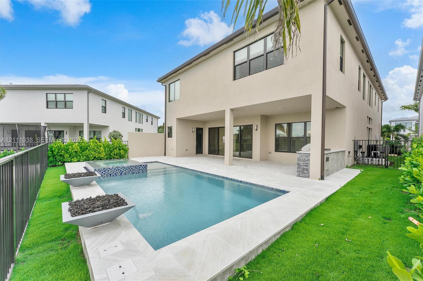 Outdoor living space featuring a covered patio, built-in stone-finish grill station, swimming pool with integrated spa, and two spill-over water features