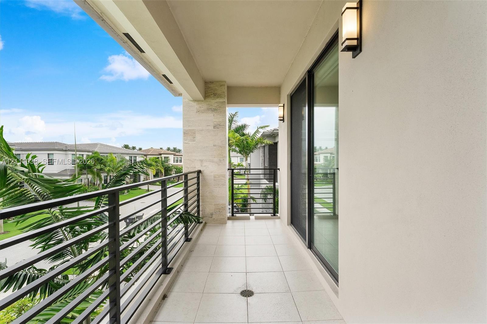 Covered balcony featuring large-format tile flooring, stone-clad pillar, metal horizontal railing, and wall-mounted exterior light fixtures