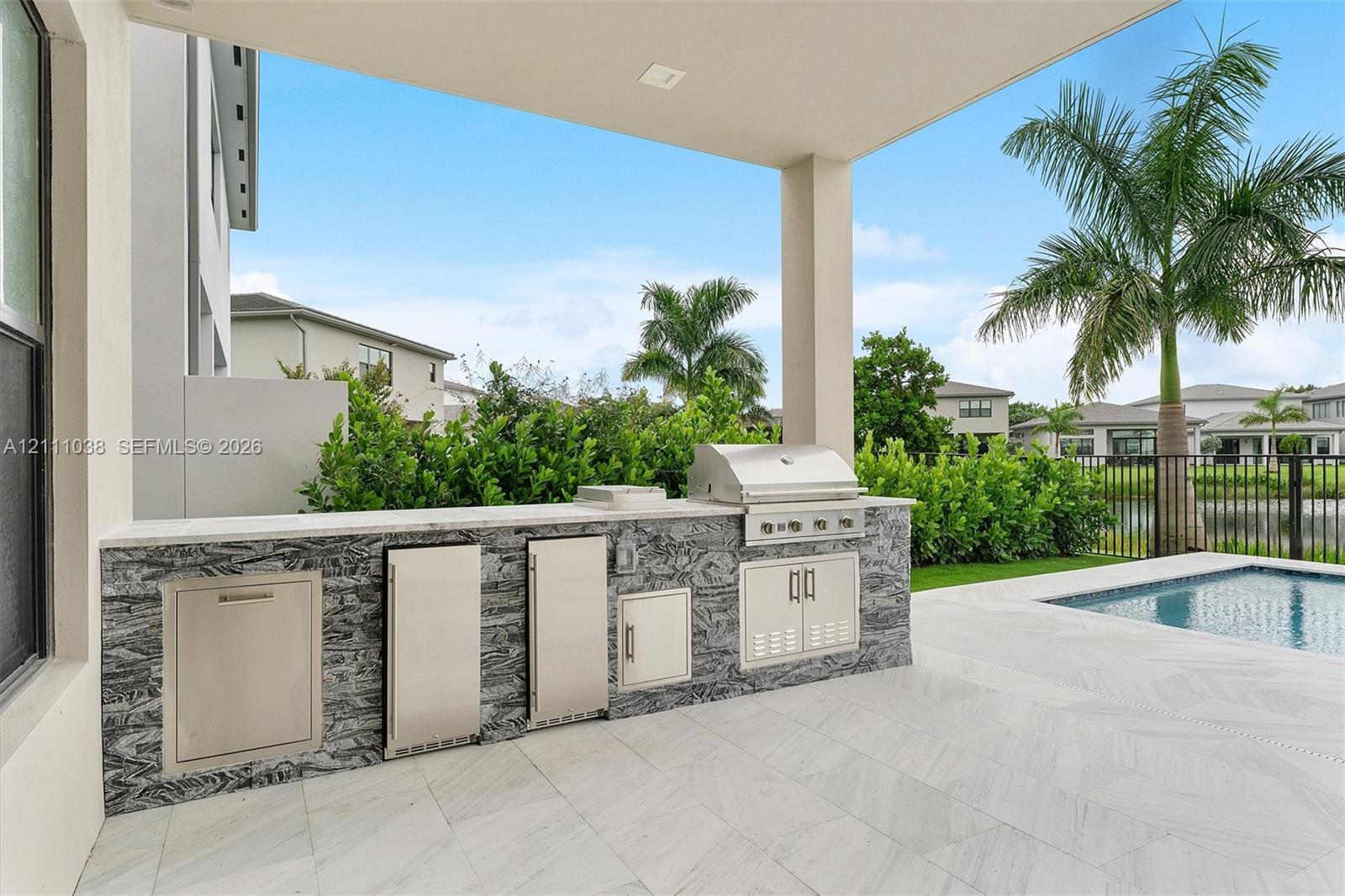 Covered patio featuring an outdoor kitchen with stainless steel appliances, stone-patterned cabinetry, stone countertops, and a swimming pool