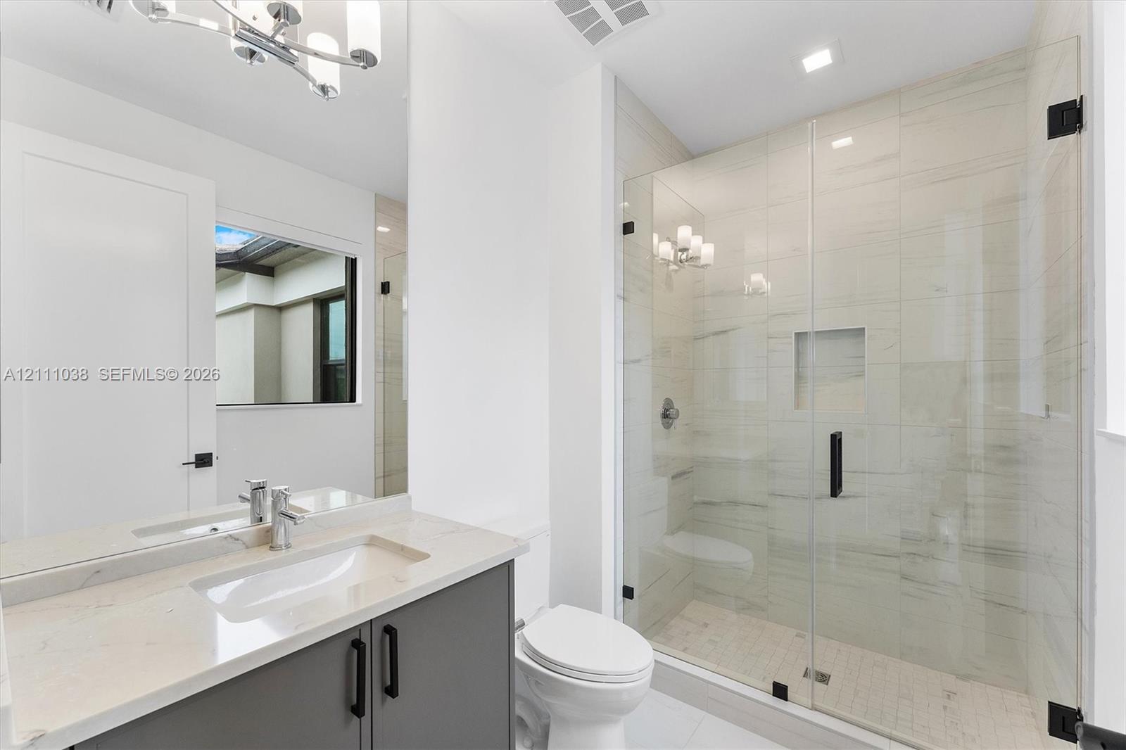 Bathroom featuring a vanity with stone-finish countertop, undermount sink, frameless glass-enclosed shower with floor-to-ceiling tile, and matte black hardware