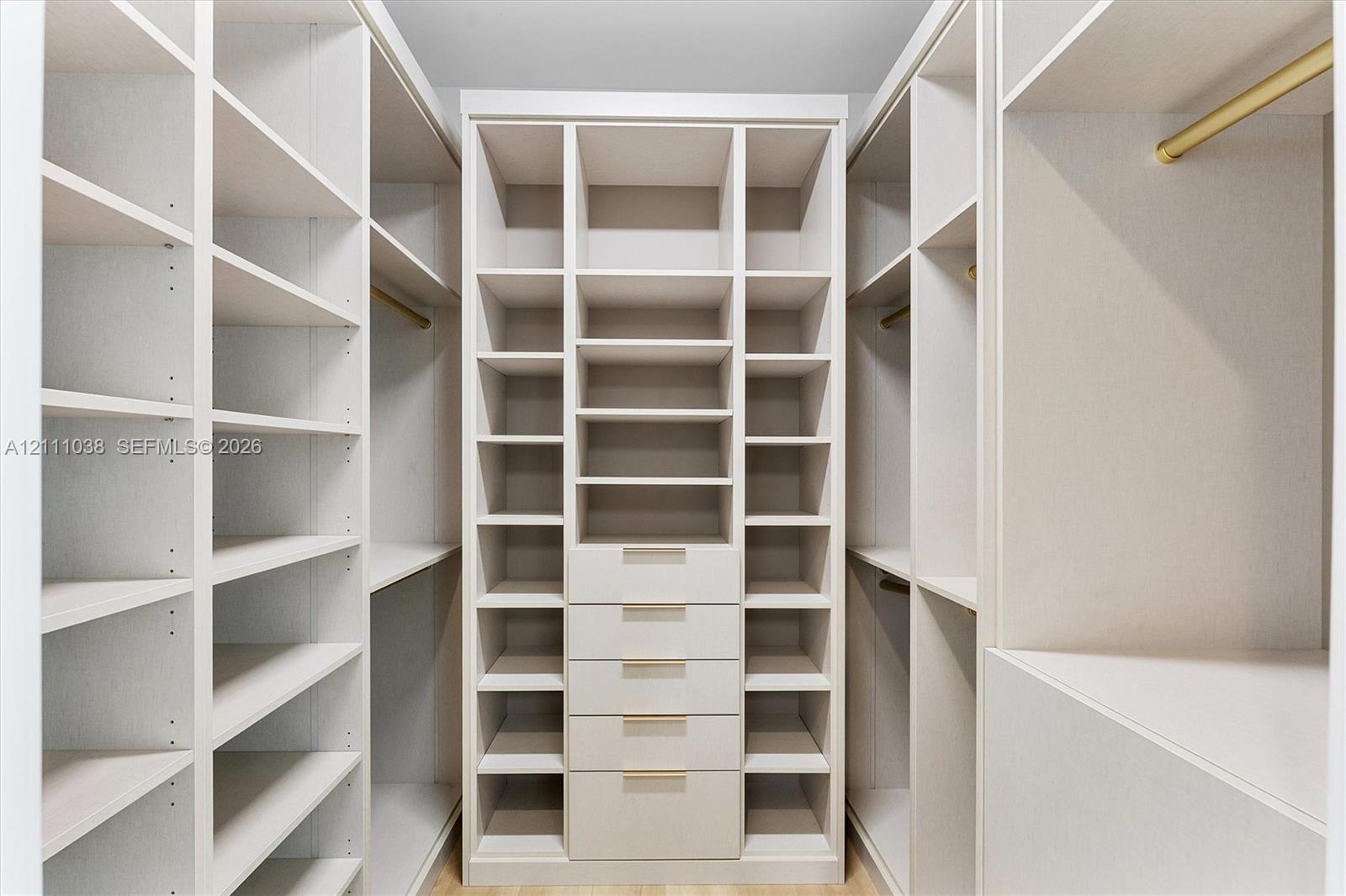 Custom walk-in closet featuring extensive built-in shelving, a five-drawer dresser unit, integrated garment rods with brass-tone hardware, and light-toned cabinetry