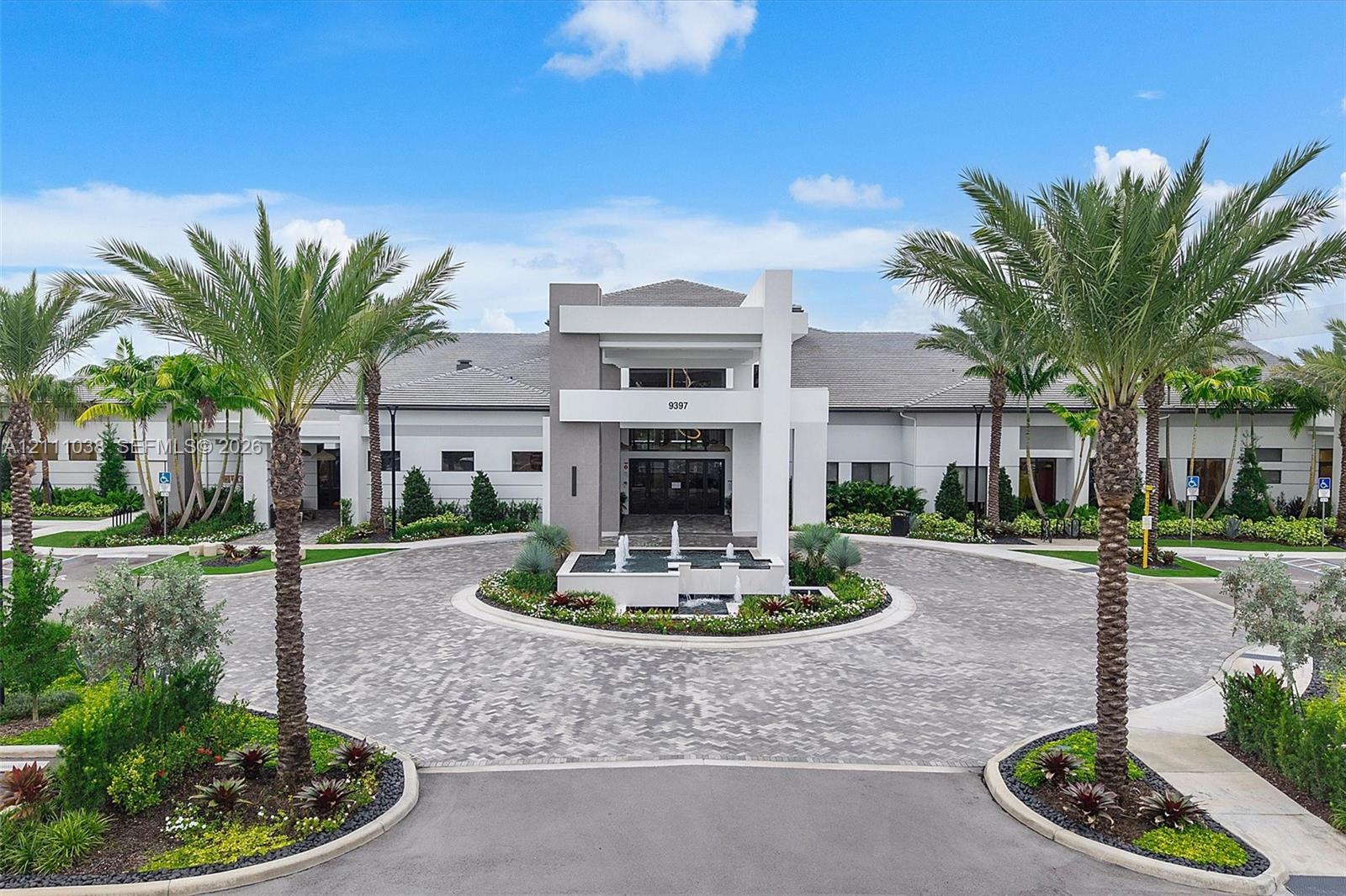 Contemporary exterior featuring a structured geometric entryway, a circular paver driveway, a central water feature, and mature palm landscaping