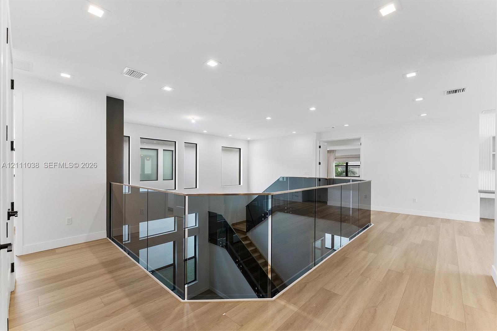 Open landing featuring wood-finish flooring, recessed lighting, and a frameless glass railing system