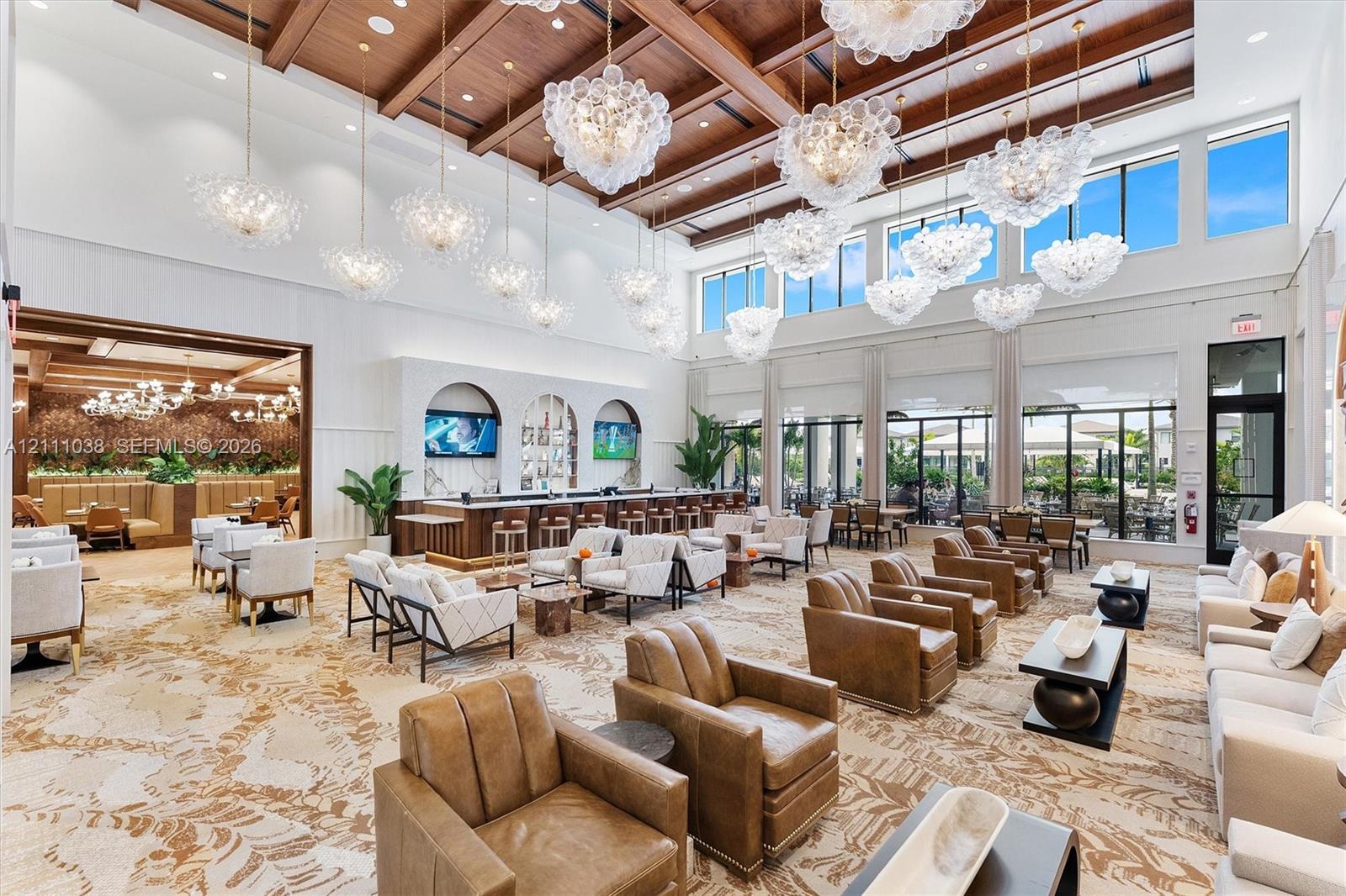 Expansive gathering hall featuring a vaulted ceiling with exposed wood beams, a series of multi-tiered glass chandeliers, a built-in bar with arched shelving, and floor-to-ceiling windows