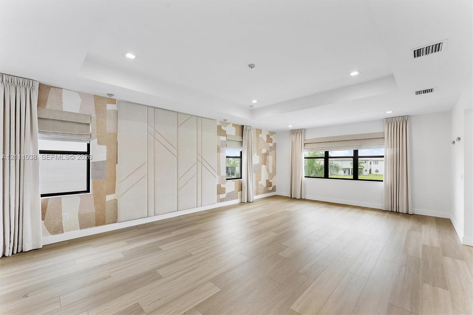 Tray ceiling featuring recessed lighting, light wood-finish flooring, and wall panels with textured geometric detailing