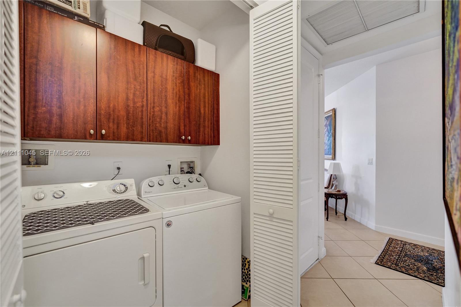Laundry area featuring wood-finish wall-mounted cabinetry, louvered bi-fold closet doors, and ceramic tile flooring