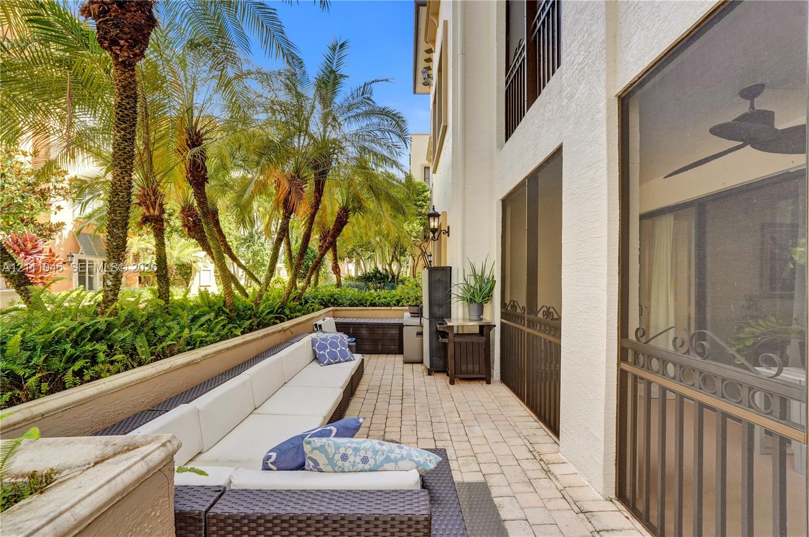 Covered patio featuring paver flooring, a ceiling fan, screen enclosures, and a low concrete retaining wall surrounded by mature landscaping