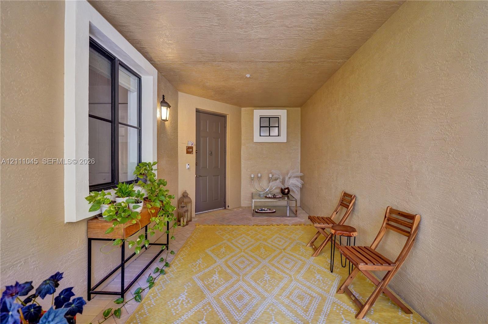 Covered entryway featuring textured stucco walls, a multi-pane window with black framing, a square accent window, and an attached exterior wall-mounted light fixture