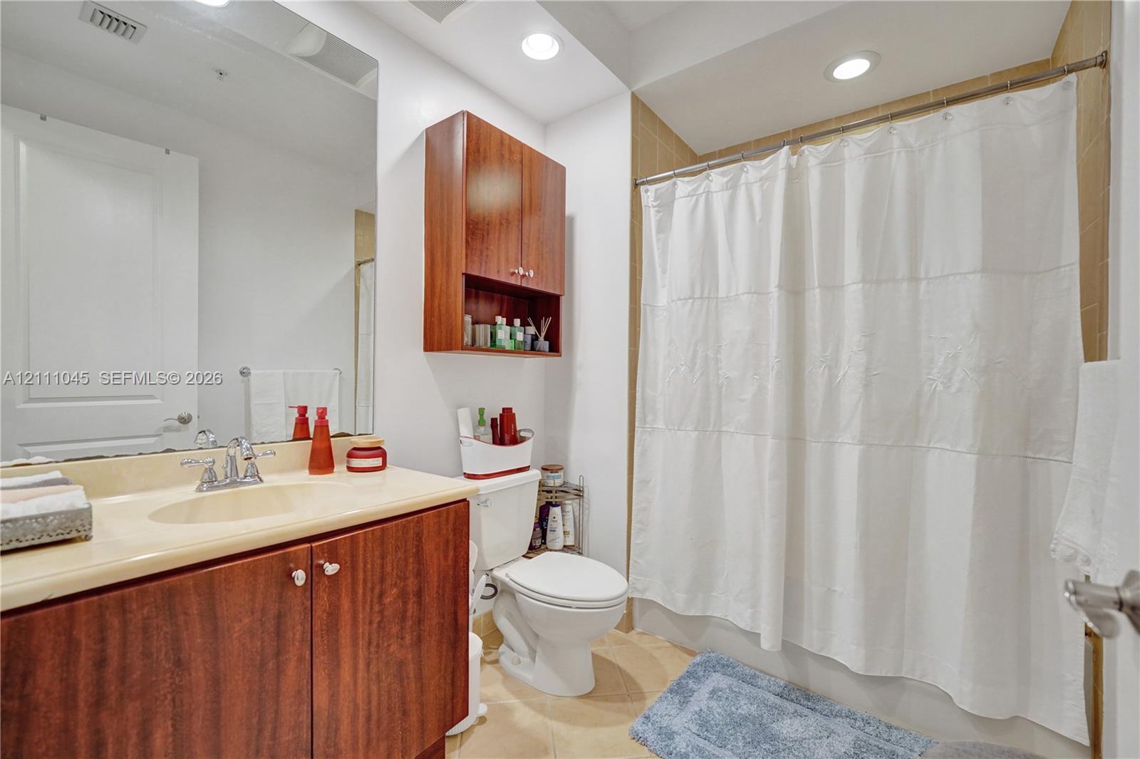 Bathroom featuring wood-finish cabinetry, a seamless countertop with an integrated sink, a wall-mounted storage cabinet, and recessed ceiling lighting