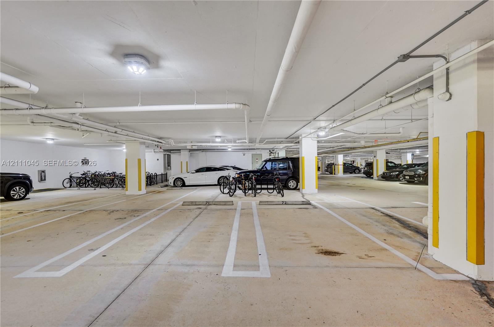 Covered parking garage featuring concrete flooring, designated stalls with painted line markings, structural columns, and integrated bicycle racks