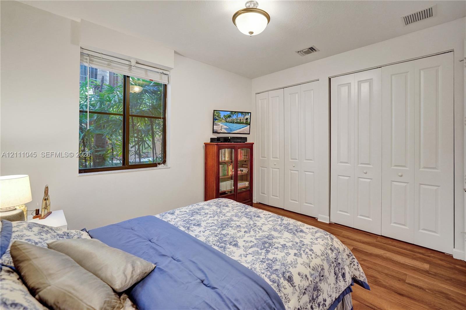 Bedroom featuring wood-finish flooring, dual bi-fold door closets, a large window, and a central ceiling-mounted light fixture
