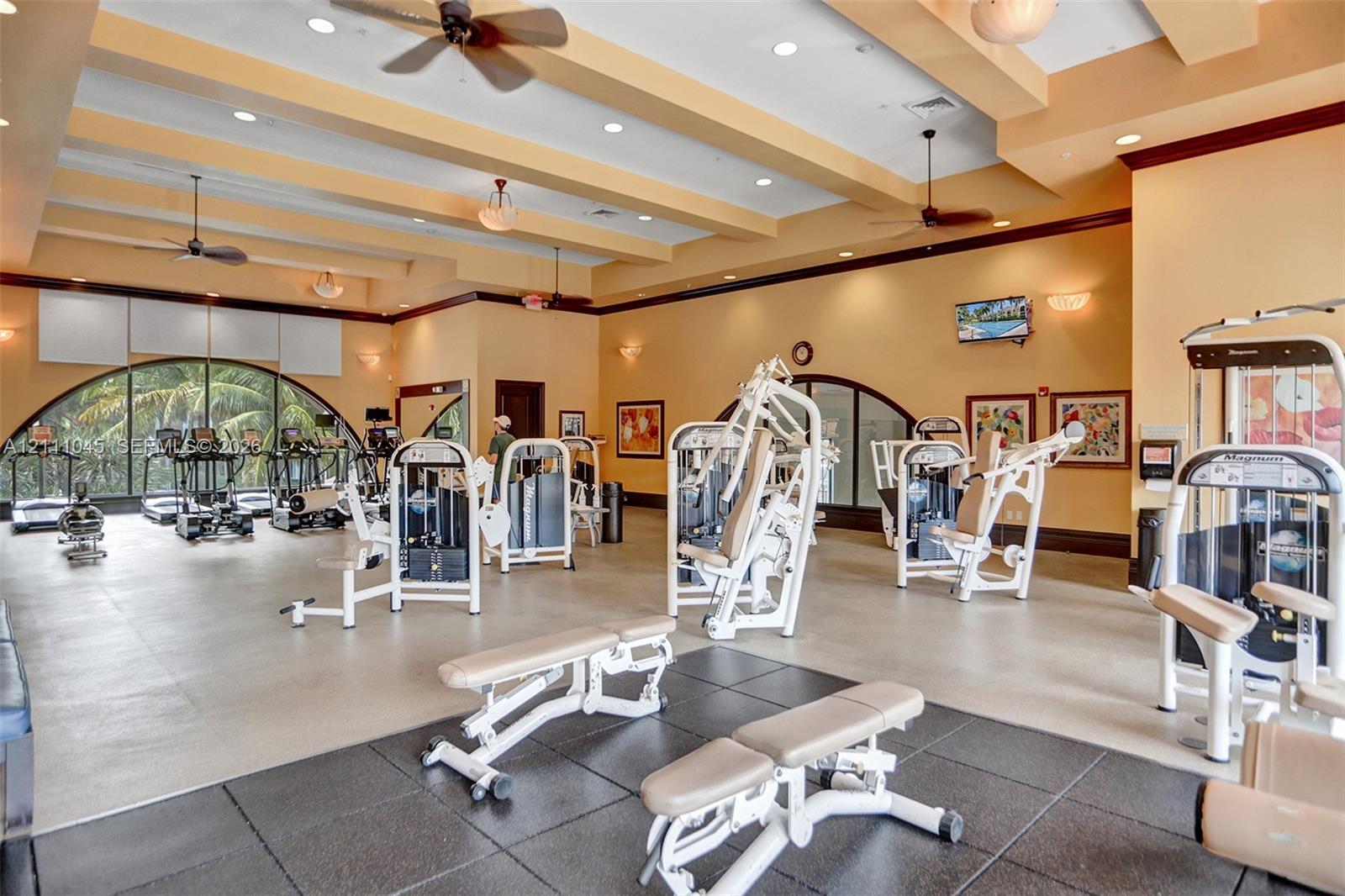 Fitness center featuring coffered ceilings, recessed lighting, multiple ceiling fans, arched windows, and multi-surface flooring