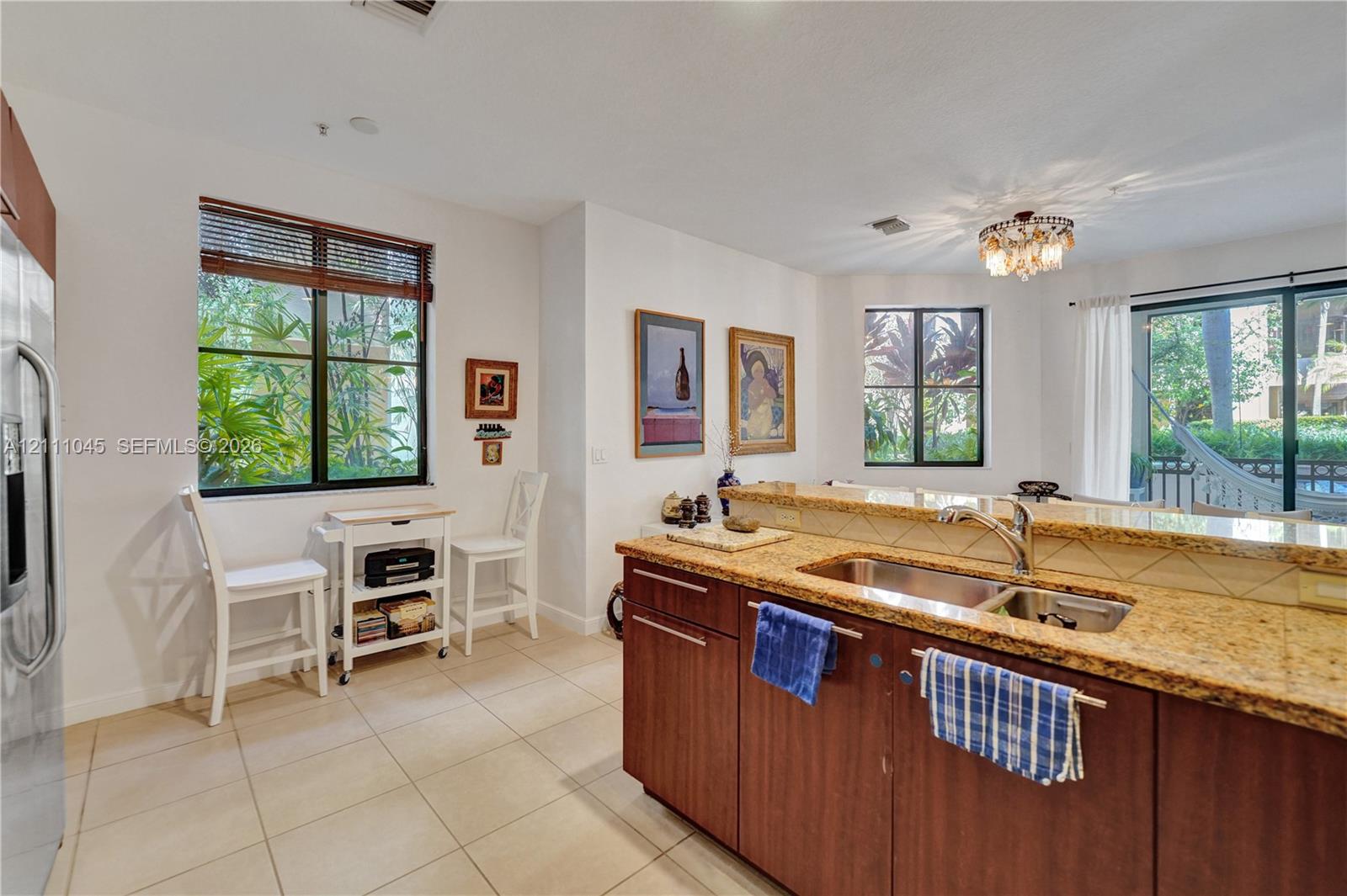 Kitchen featuring a breakfast bar with stone-surfaced countertops, a stainless steel dual-basin undermount sink, dark-finish cabinetry, and ceramic tile flooring