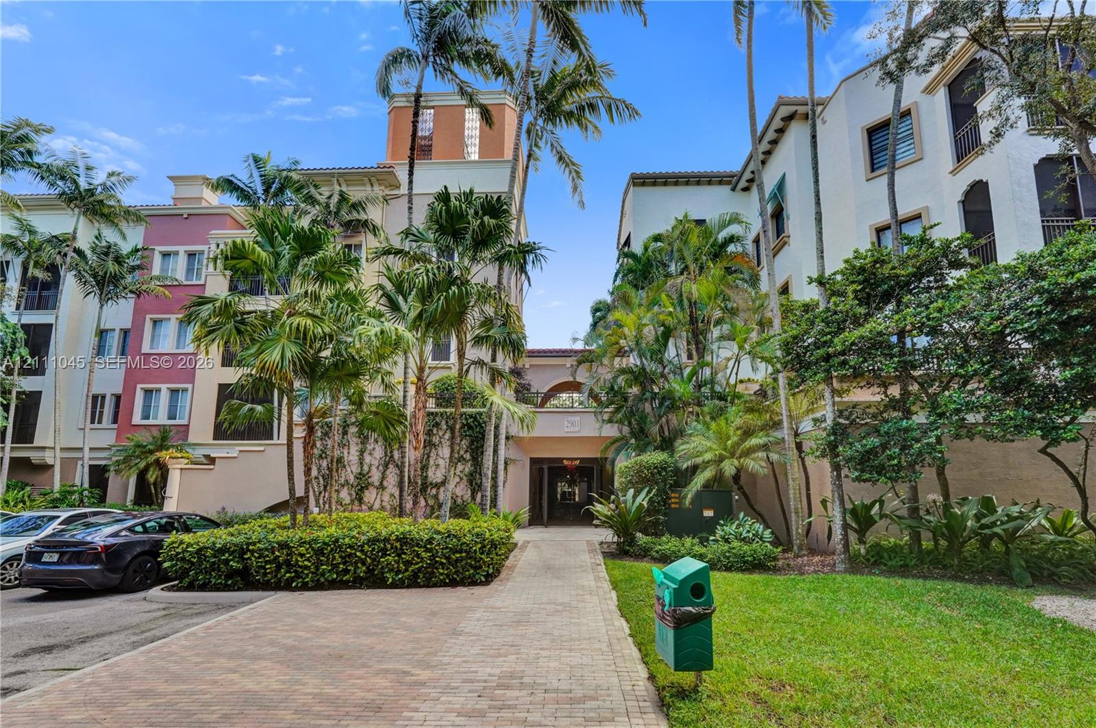 Multi-story Mediterranean-inspired exterior featuring stucco facades, arched architectural details, mature palm trees, and brick paver walkways