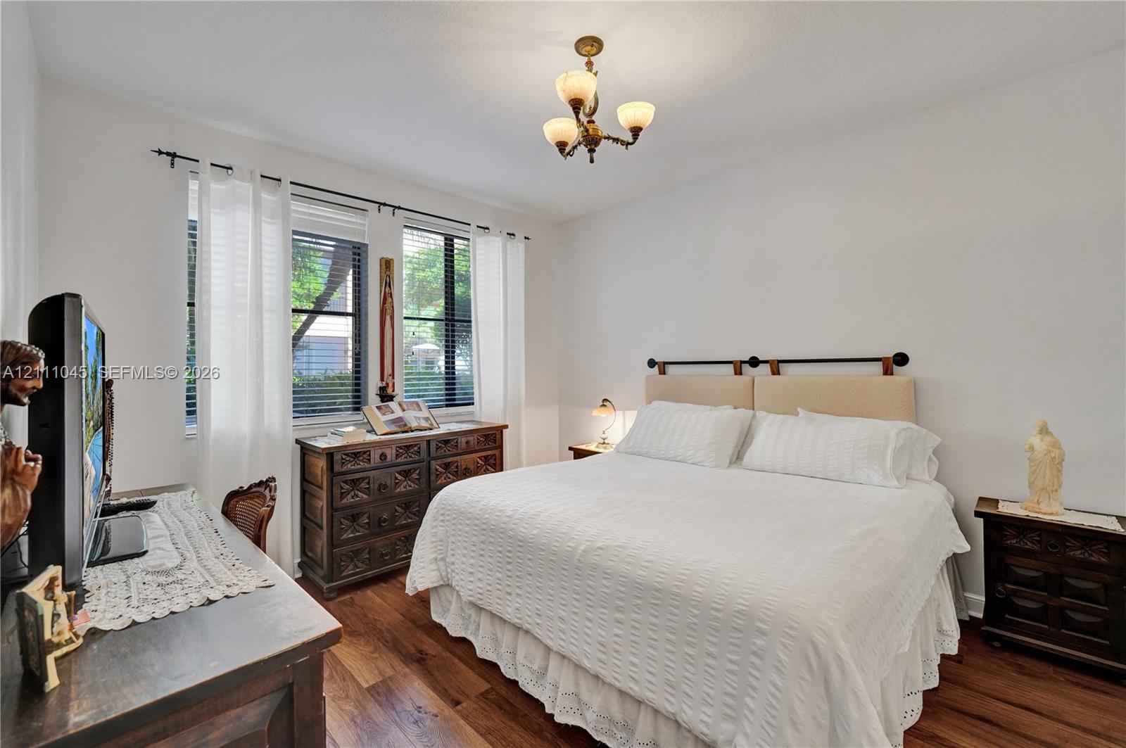 Bedroom featuring wood-finish flooring, dual windows with blinds, and a multi-arm chandelier