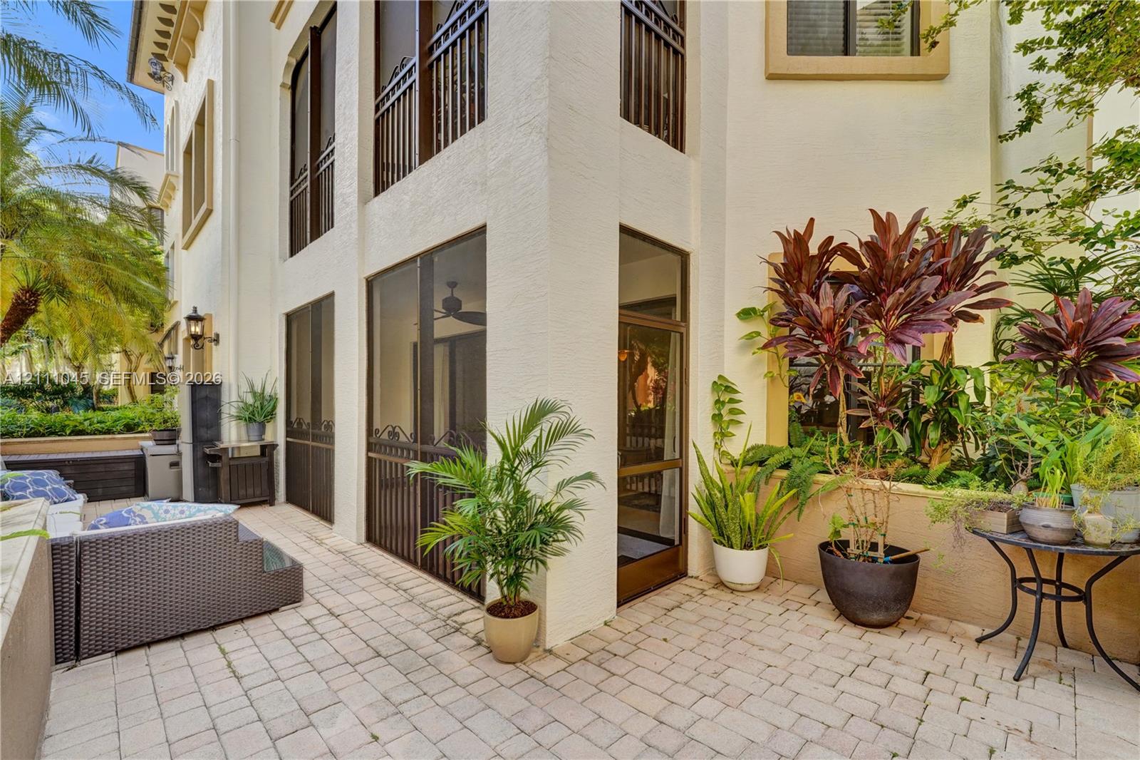 Stucco exterior featuring multiple levels, paved stone patio, screened enclosure, decorative metal railings, and attached exterior lighting