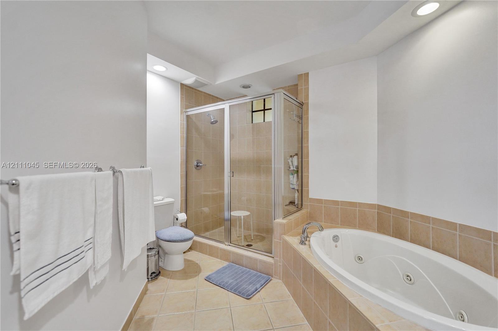 Bathroom featuring a jetted soaking tub, tiled shower enclosure with metal-framed glass door, and neutral tile flooring