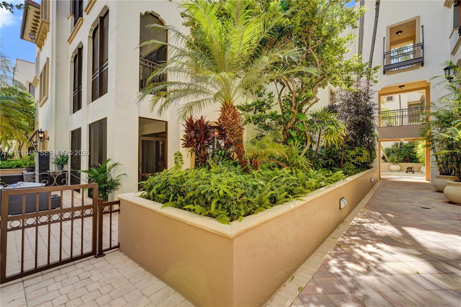 Mediterranean-style exterior featuring a stucco facade, raised masonry garden bed, integrated wrought-iron gate, stone-paver hardscaping, and multi-level balconies with decorative railings
