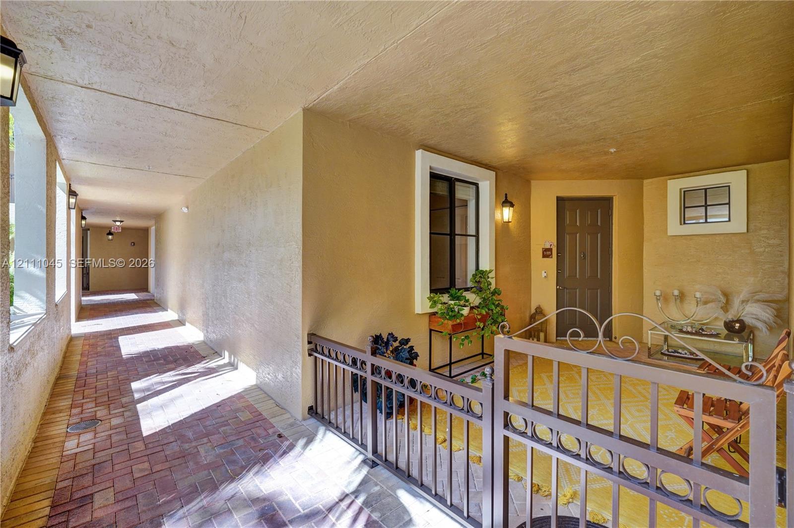 Covered entryway featuring brick pavers, decorative metal fencing, recessed lighting, and a paneled entry door