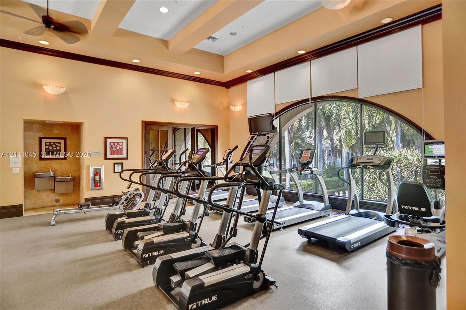 Fitness center featuring high ceilings with recessed lighting, an expansive arched window, integrated sound system, and wall-mounted water fountain