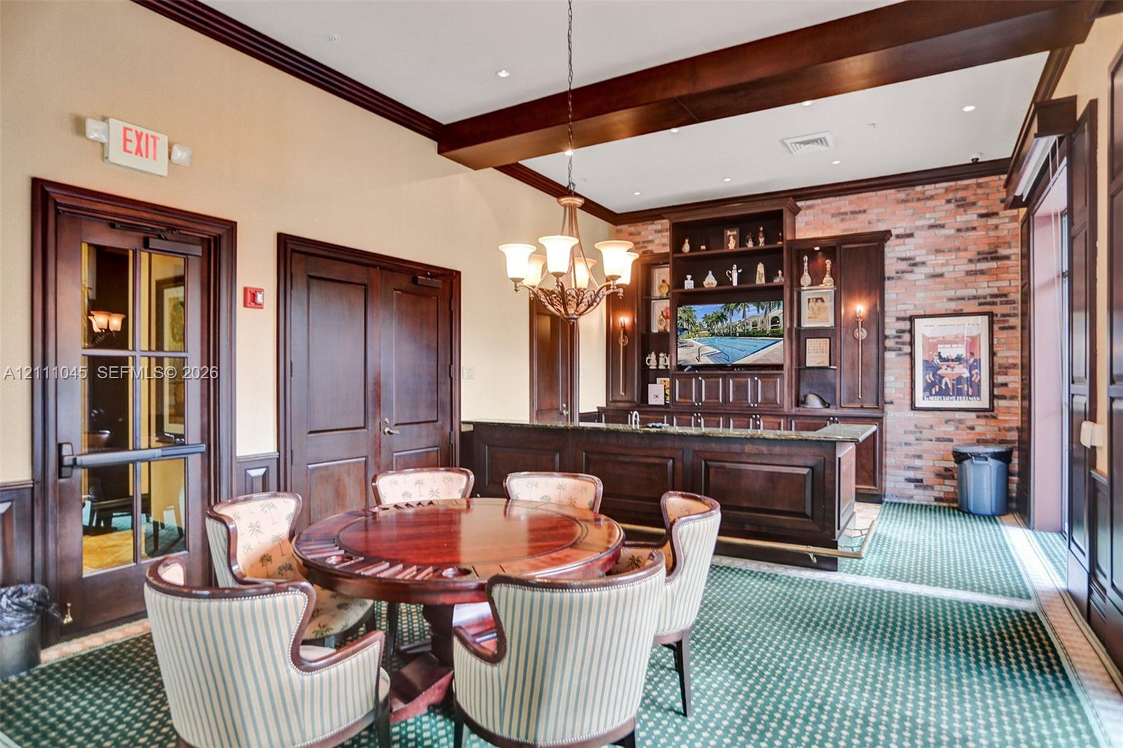 Custom built-in bar featuring dark wood cabinetry, exposed brick wall, overhead chandelier lighting, and dark wood crown molding