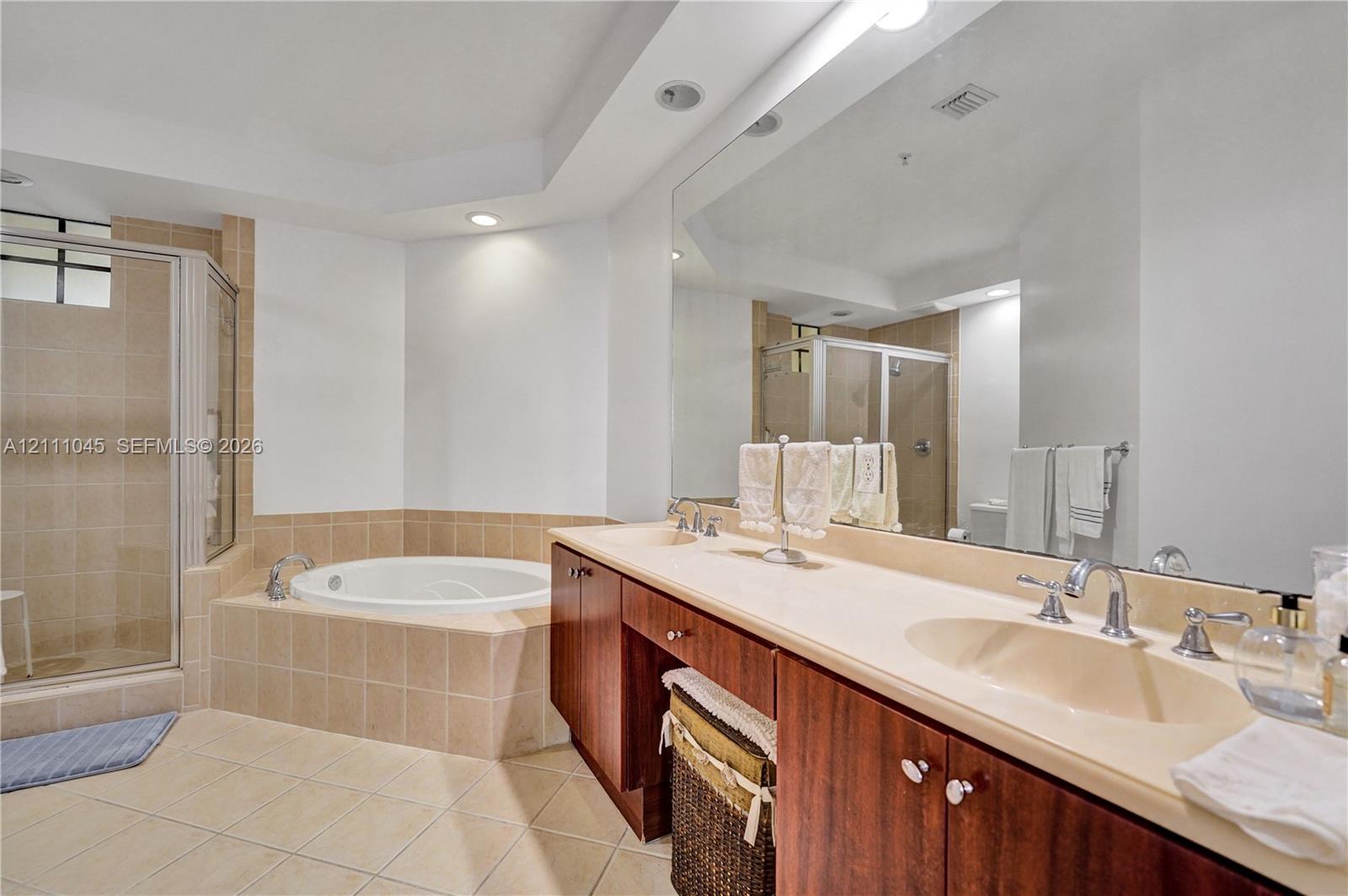 Bathroom featuring a jetted soaking tub, tiled shower enclosure, expansive dual-sink vanity with wood-finish cabinetry, and recessed lighting