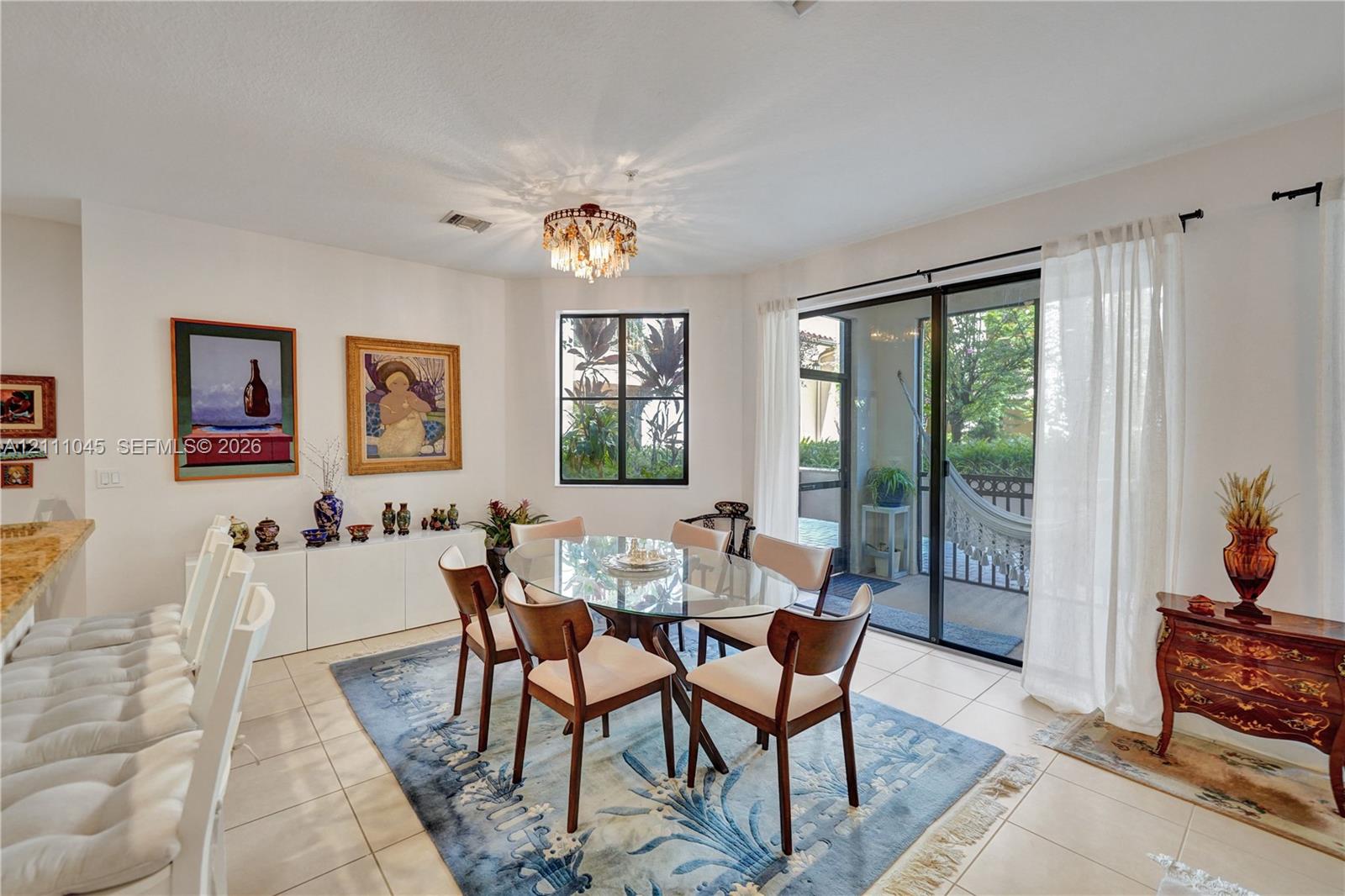 Dining area featuring large-format ceramic tile flooring, built-in cabinetry with a stone countertop, a decorative tiered chandelier, and sliding glass doors with access to a screened outdoor area