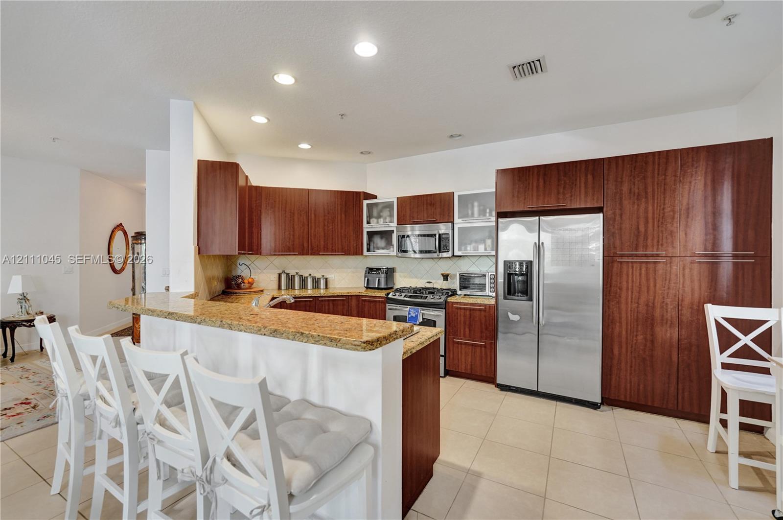 Kitchen featuring dark wood-finish cabinetry, stone-surface countertops, stainless steel appliances, recessed ceiling lighting, and tile flooring