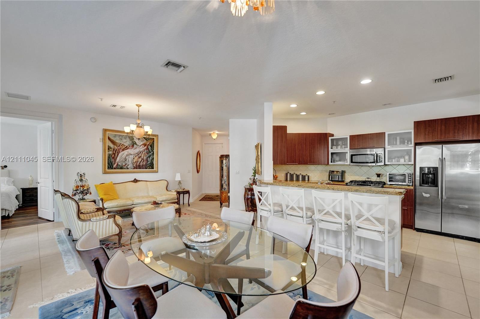 Open-concept interior featuring light-toned tile flooring, recessed ceiling lighting, a kitchen island with stone countertops, and wood-finish cabinetry
