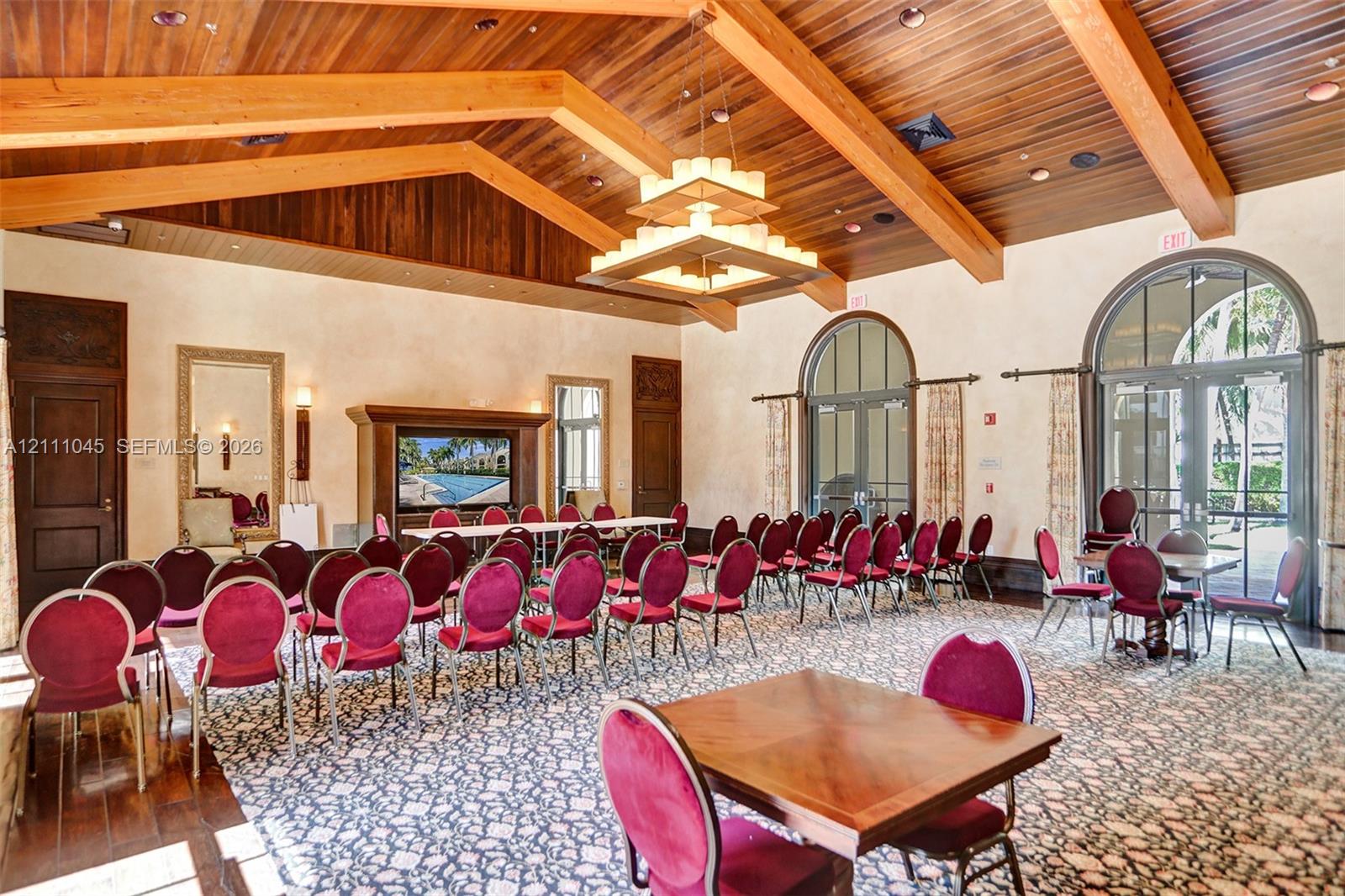 Vaulted wood-plank ceiling with exposed timber beams, tiered chandelier, built-in media cabinetry, and arched glass-paneled doors