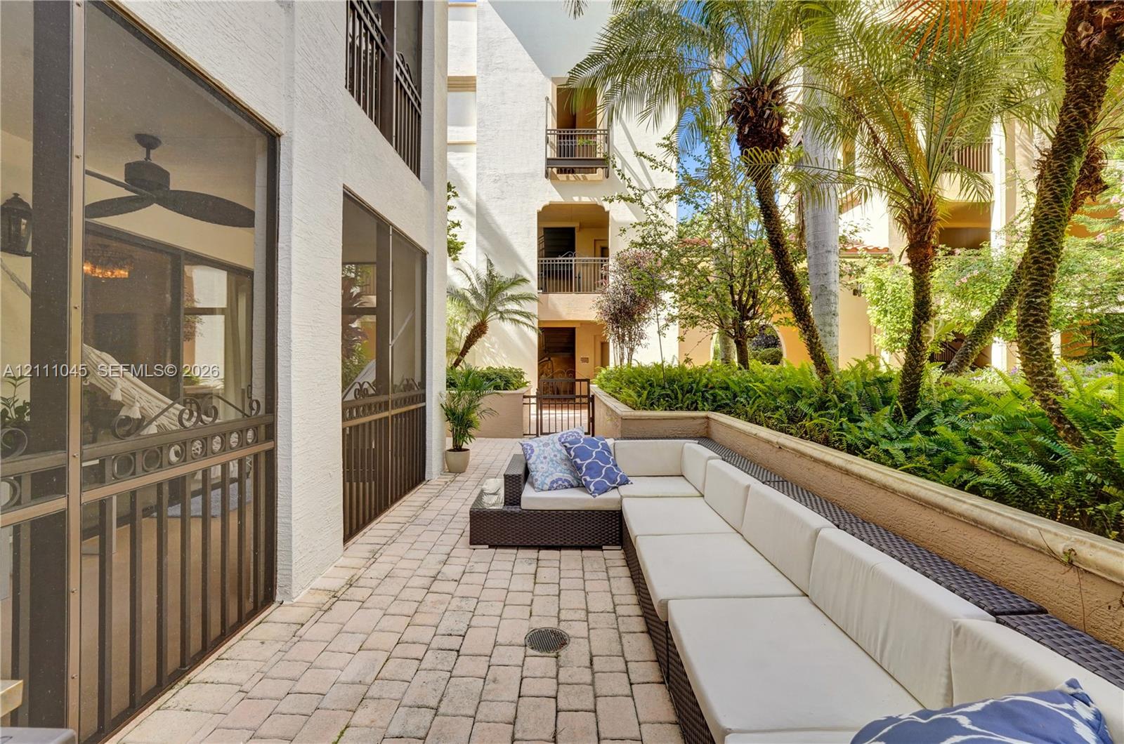 Paver-stone patio featuring a low masonry perimeter wall, screened-in enclosure, and integrated tropical landscaping