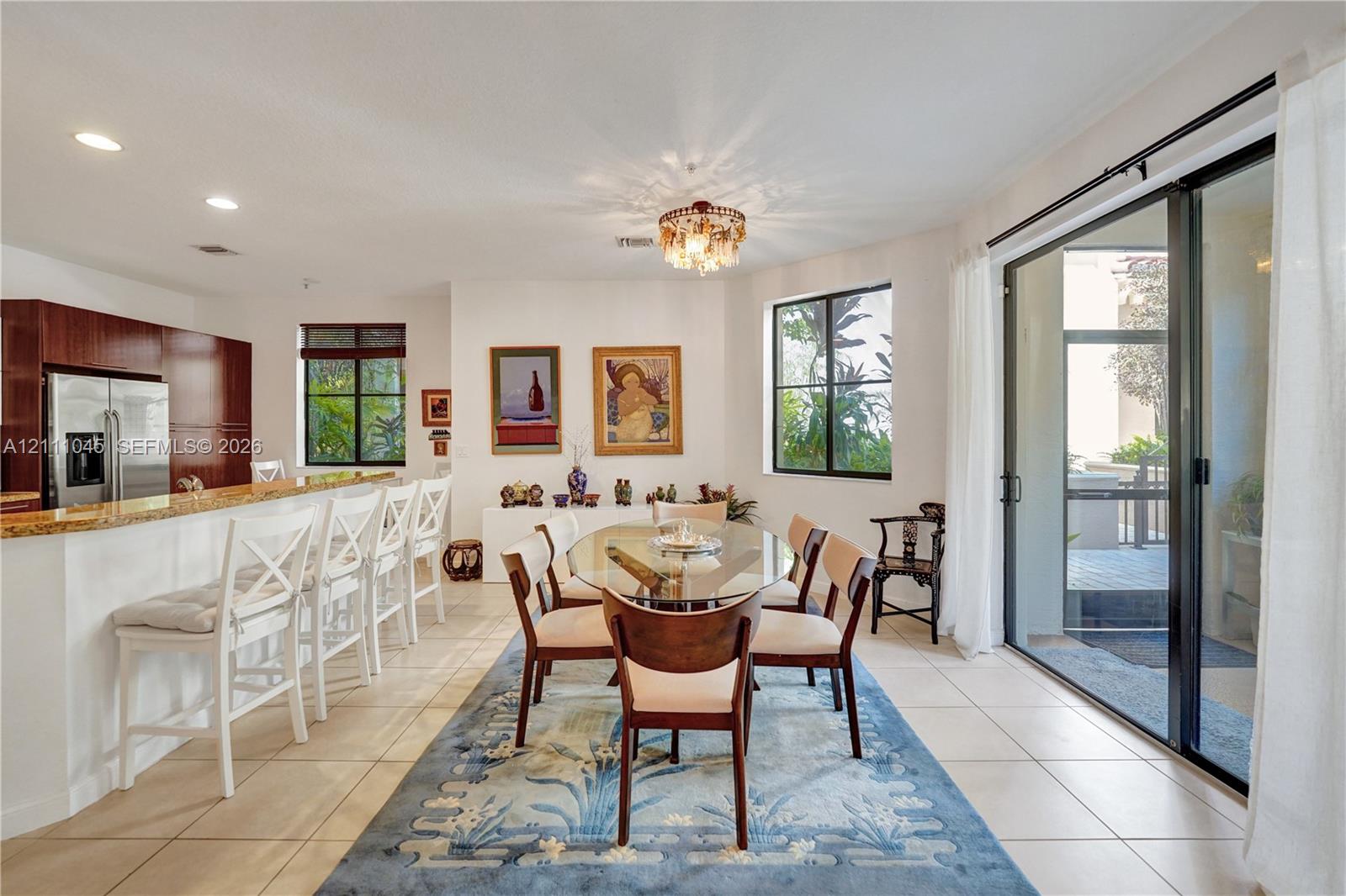 Open-concept kitchen and dining area featuring a tiered stone-top breakfast bar, tile flooring, recessed lighting, and large sliding glass doors