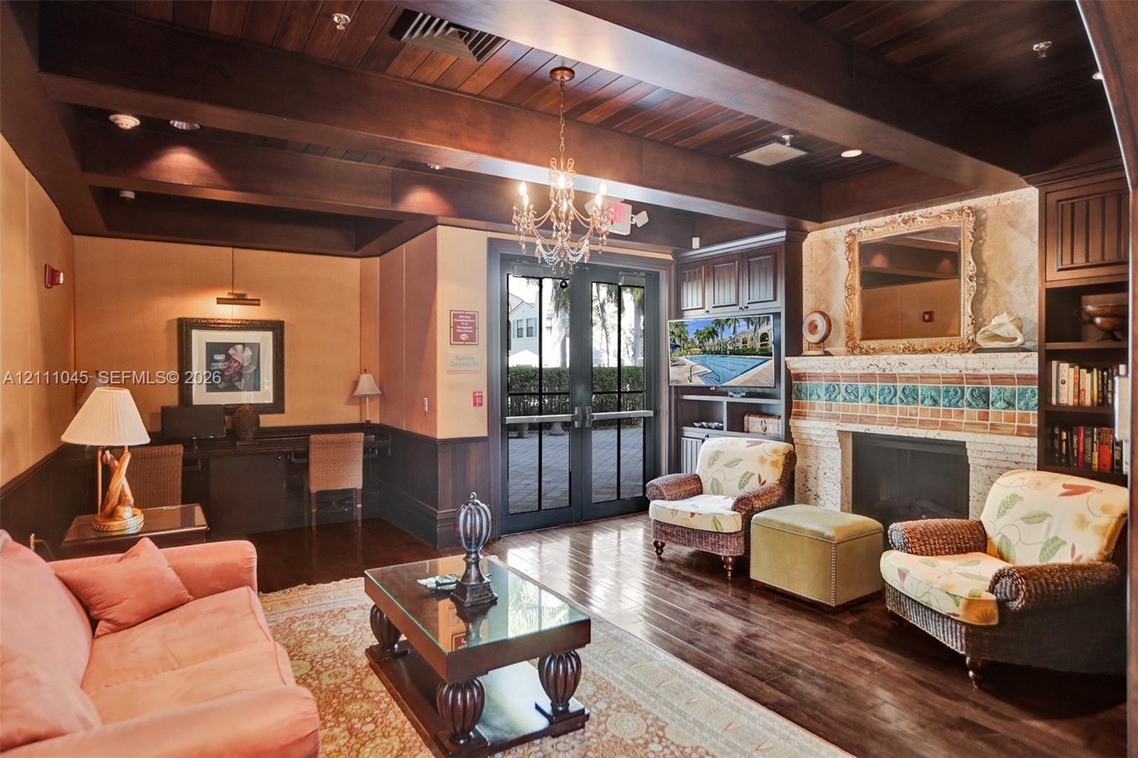 Wood-finish coffered ceiling with exposed beams, wood-finish flooring, masonry fireplace with decorative tile surround, built-in wooden cabinetry, and French-style glass paneled doors