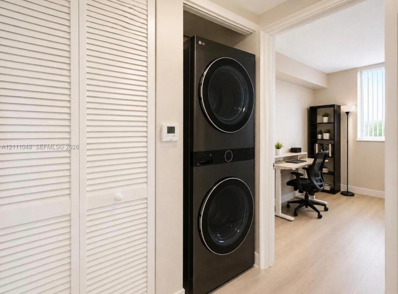 Integrated laundry closet featuring a stacked washer and dryer unit, louvered bi-fold doors, and wood-finish flooring Integrated laundry closet featuring a stacked washer and dryer unit, louvered bi-fold doors, and wood-finish flooring