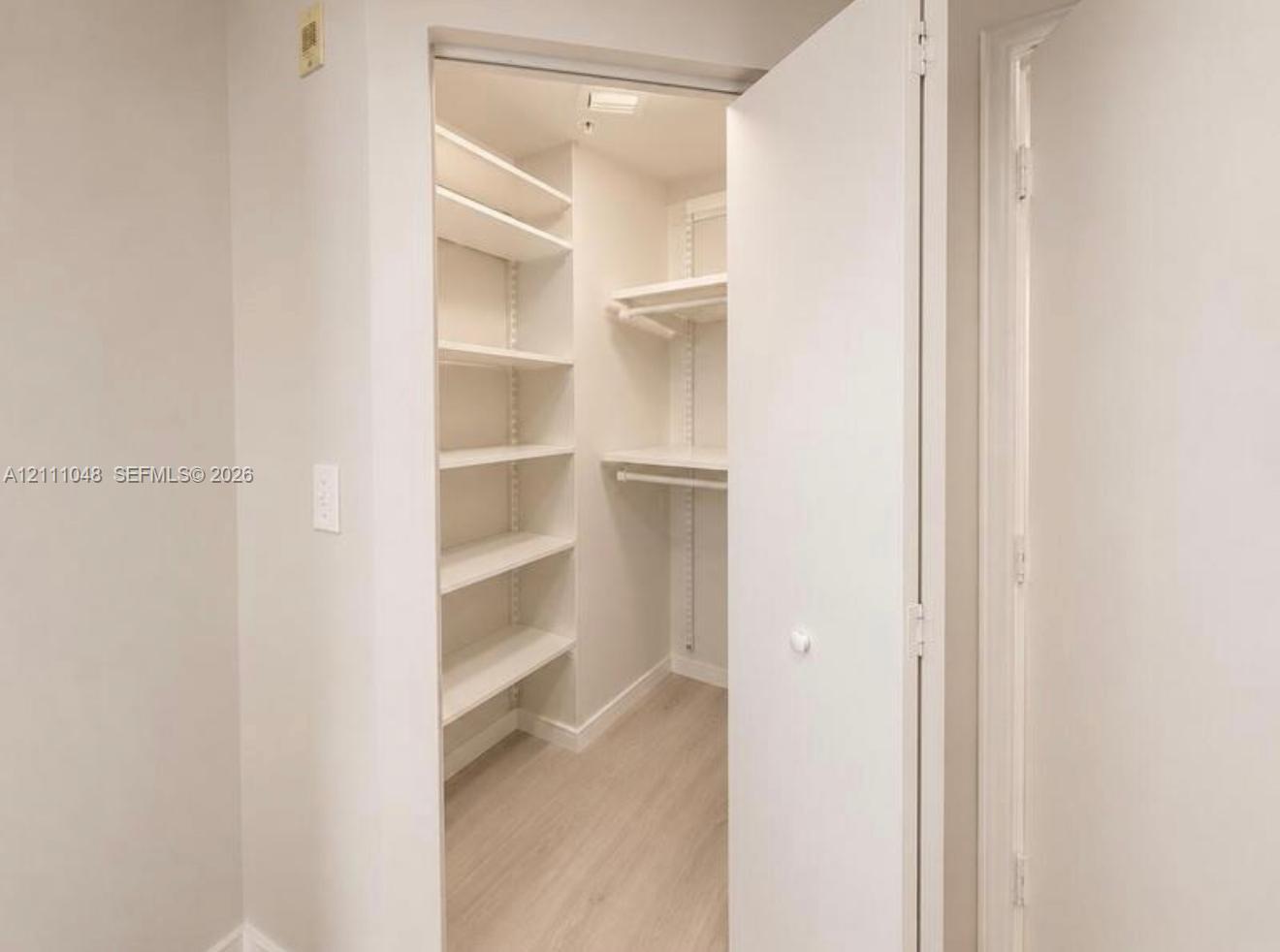 Reach-in closet featuring adjustable shelving, integrated hanging rods, and light-toned wood-finish flooring Reach-in closet featuring adjustable shelving, integrated hanging rods, and light-toned wood-finish flooring