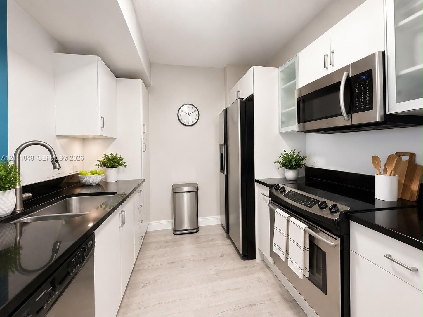 Kitchen featuring white flat-panel cabinetry, dark solid-surface countertops, wood-finish flooring, and a stainless steel appliance suite including a built-in microwave and range Kitchen featuring white flat-panel cabinetry, dark solid-surface countertops, wood-finish flooring, and a stainless steel appliance suite including a built-in microwave and range