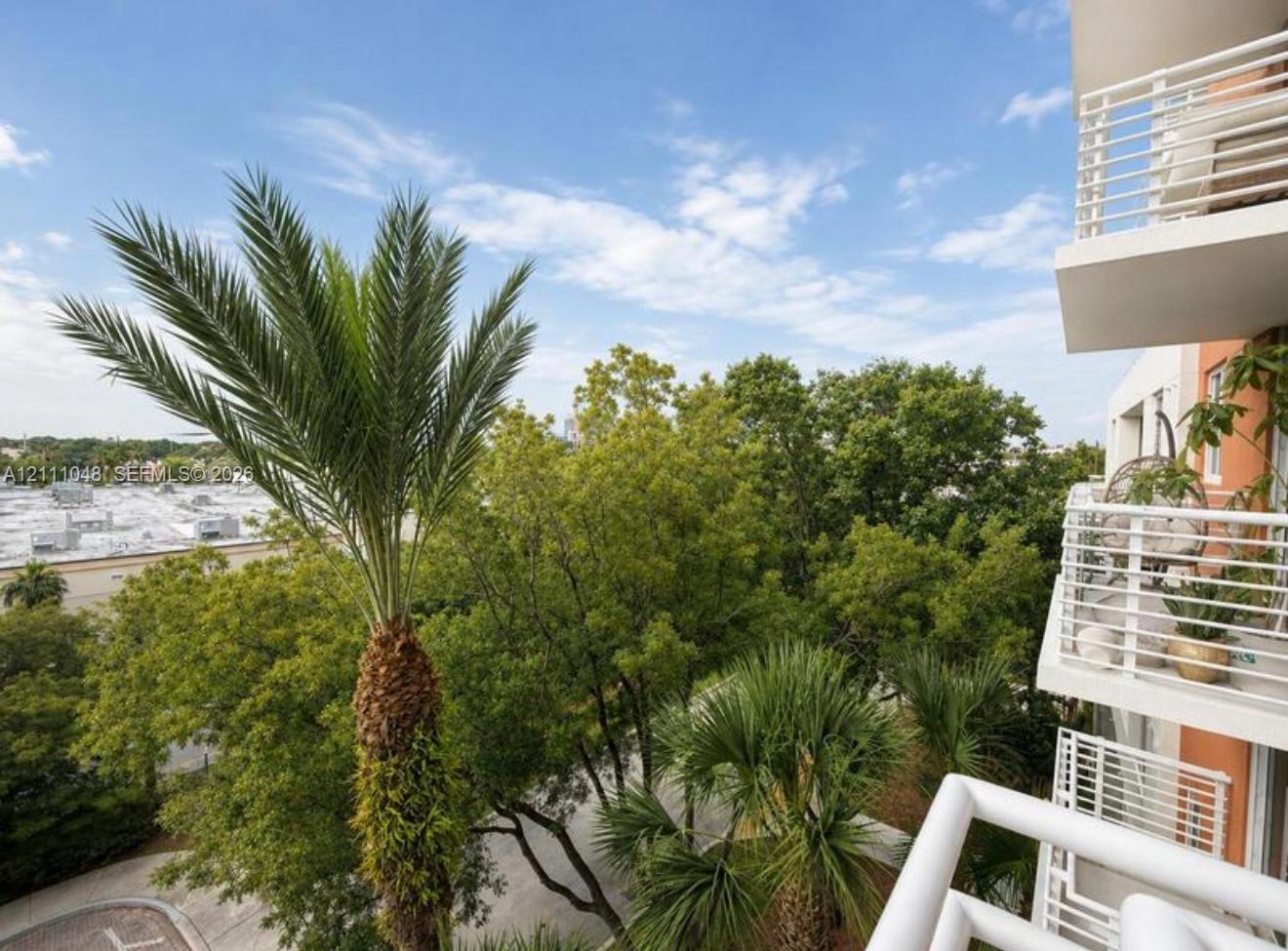 Elevated balconies with white metal railings and mature palm tree landscaping