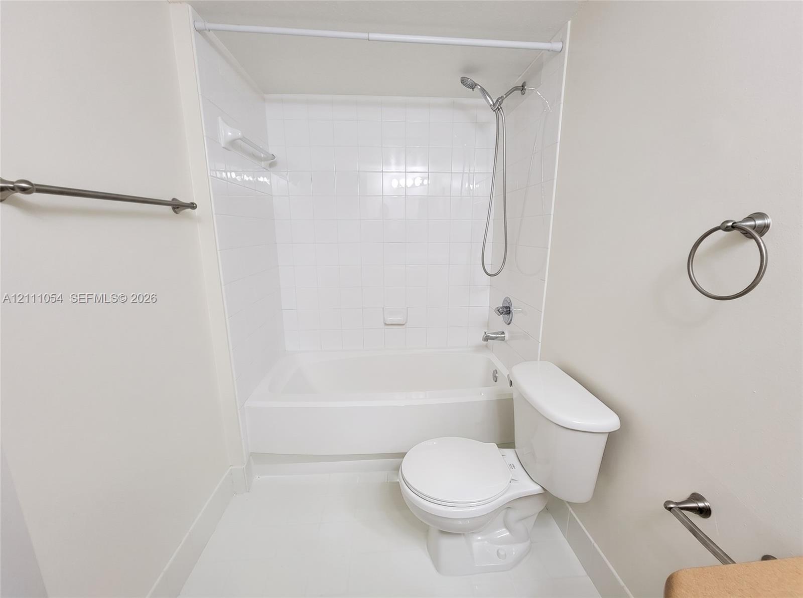 Bathroom featuring a tub-shower combination with white ceramic tile surround, a handheld showerhead, a two-piece toilet, and polished metal hardware