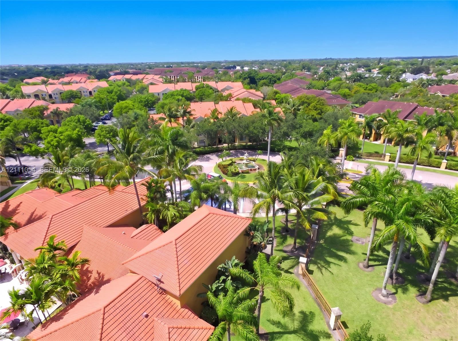 Aerial perspective of terracotta-tiled rooflines, expansive manicured grounds, mature palm trees, and a decorative central fountain