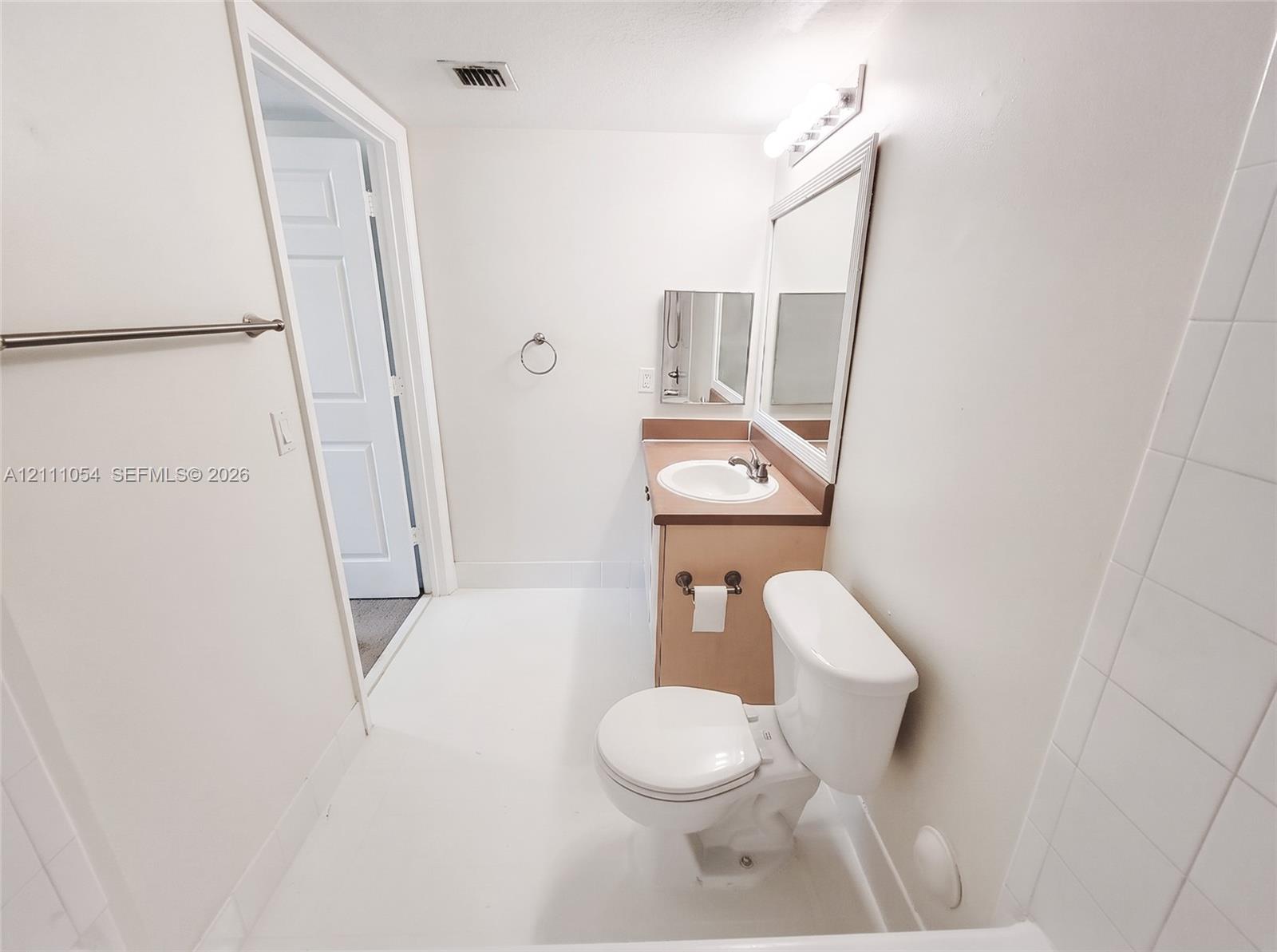 Bathroom featuring a vanity with integrated sink, rectangular wall-mounted mirror, overhead vanity lighting, and wall-mounted towel bar