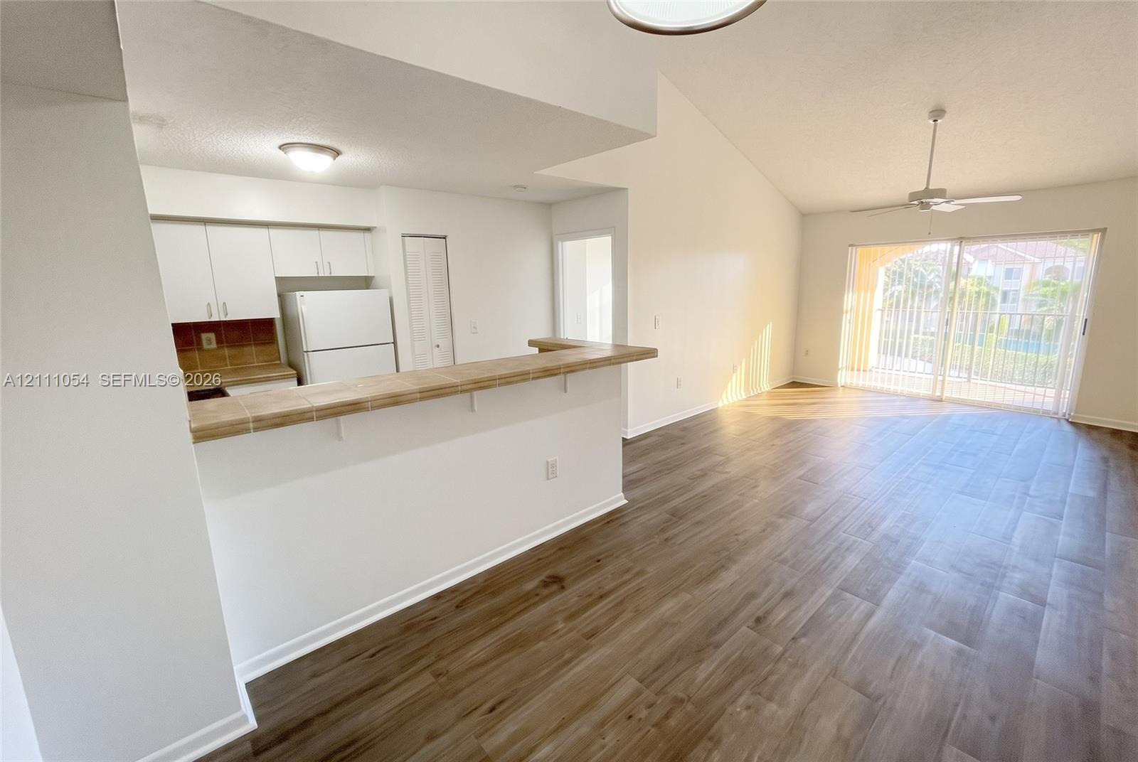 Open-concept kitchen featuring a tile-topped breakfast bar, wood-finish flooring, vaulted ceilings, and glass sliding doors